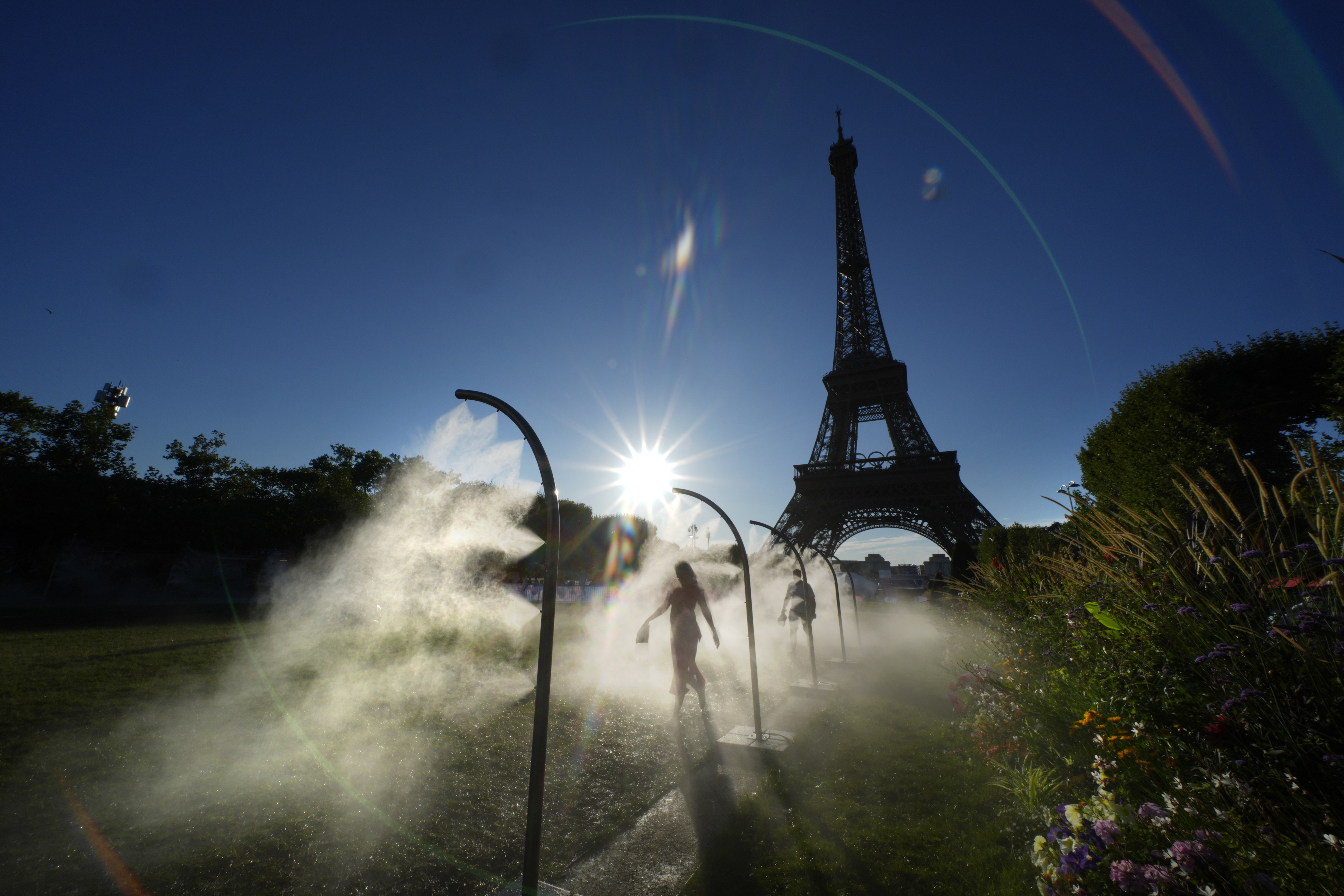 A spectator walks through a water mist sprayers on her way to Eiffel Tower Stadium to watch a beach volleyball at the 2024 Summer Olympics, Sunday, July 28, 2024, in Paris, France. 