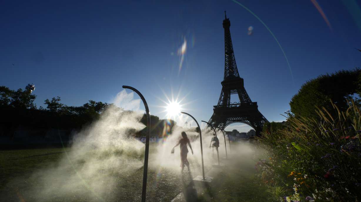 A spectator walks through a water mist sprayers on her way to Eiffel Tower Stadium to watch a beach volleyball at the 2024 Summer Olympics, Sunday, July 28, 2024, in Paris, France.