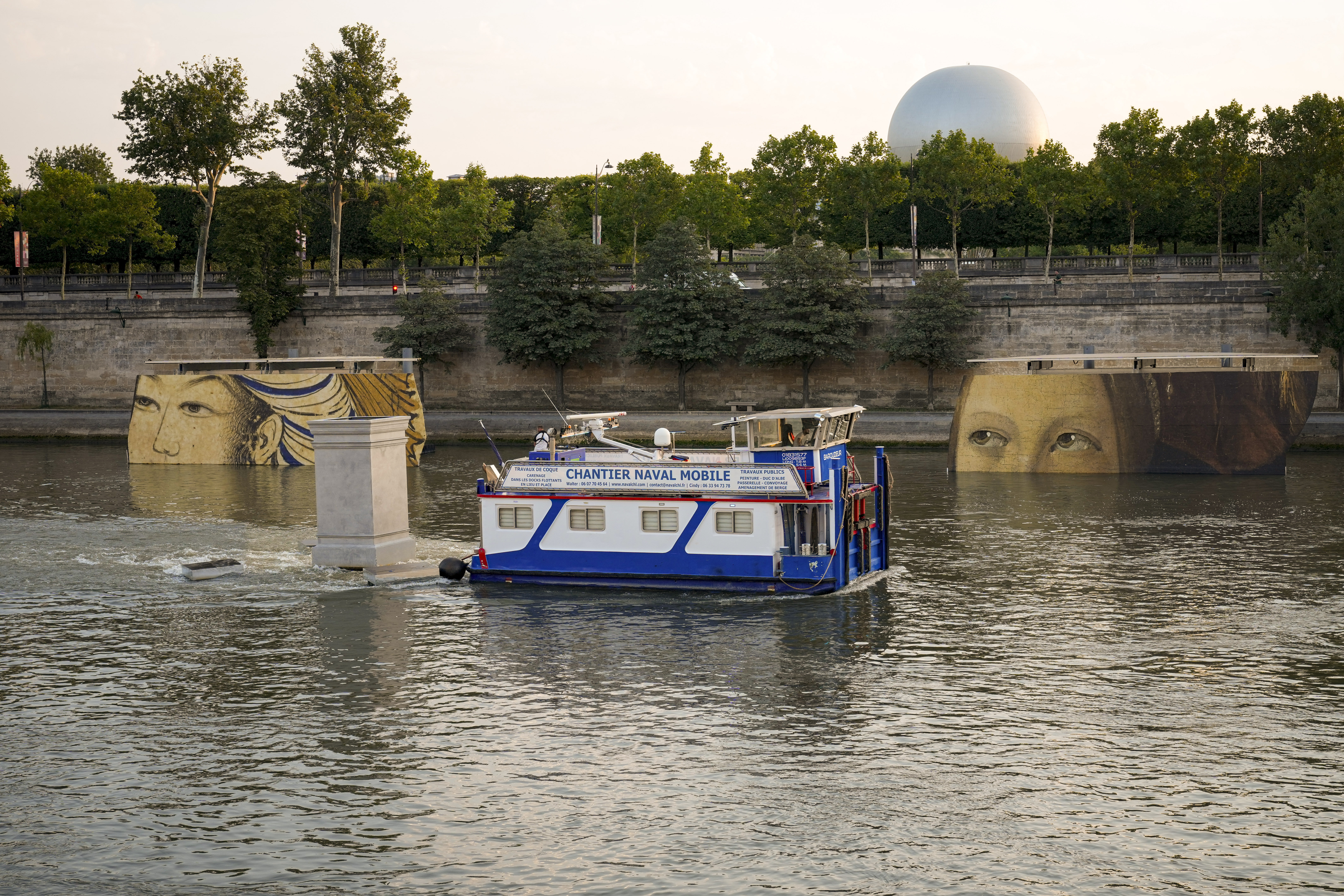 A boat sails past reproductions of artworks decorating the banks of the River Seineat the 2024 Summer Olympics, Tuesday, July 30, 2024, in Paris, France. The men's Olympic triathlon has been postponed over concerns about water quality in Paris' Seine River, where the swimming portion of the race was supposed to take place. 