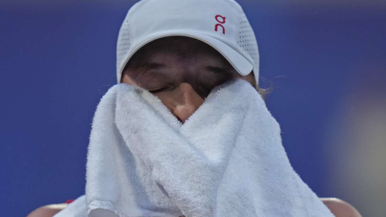Iga Swiatek of Poland wipes her sweat as she plays Wang Xiyu of China during their women's singles third round match at the Roland Garros stadium, at the 2024 Summer Olympics, Tuesday, July 30, 2024, in Paris, France.