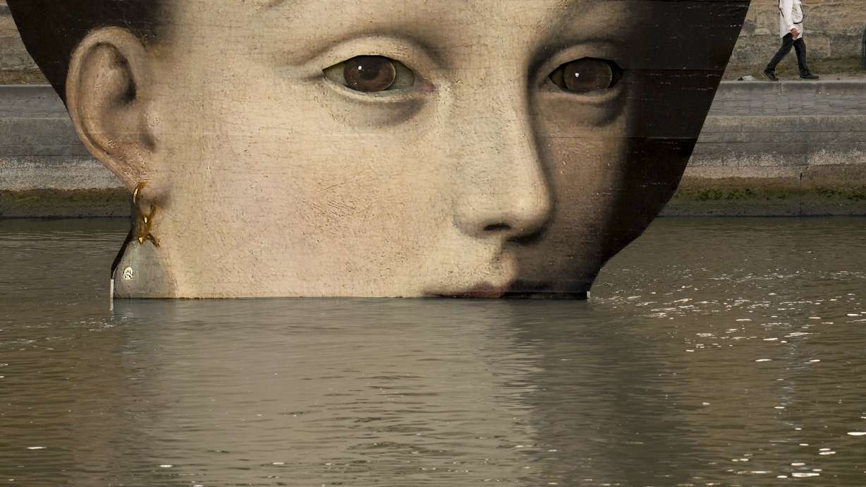 A man wipes his face as he walks past reproductions of artworks decorating the banks of the River Seineat the 2024 Summer Olympics, Tuesday, July 30, 2024, in Paris, France. The men's Olympic triathlon has been postponed over concerns about water quality in Paris' Seine River, where the swimming portion of the race was supposed to take place.