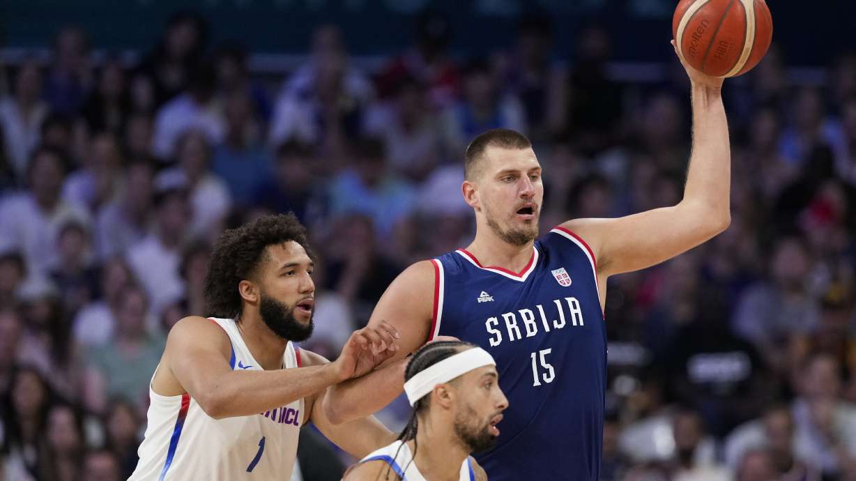 Nikola Jokic, of Serbia, looks to pass away from George Conditt IV, of Puerto Rico, in a men's basketball game at the 2024 Summer Olympics, Wednesday, July 31, 2024, in Villeneuve-d'Ascq, France.