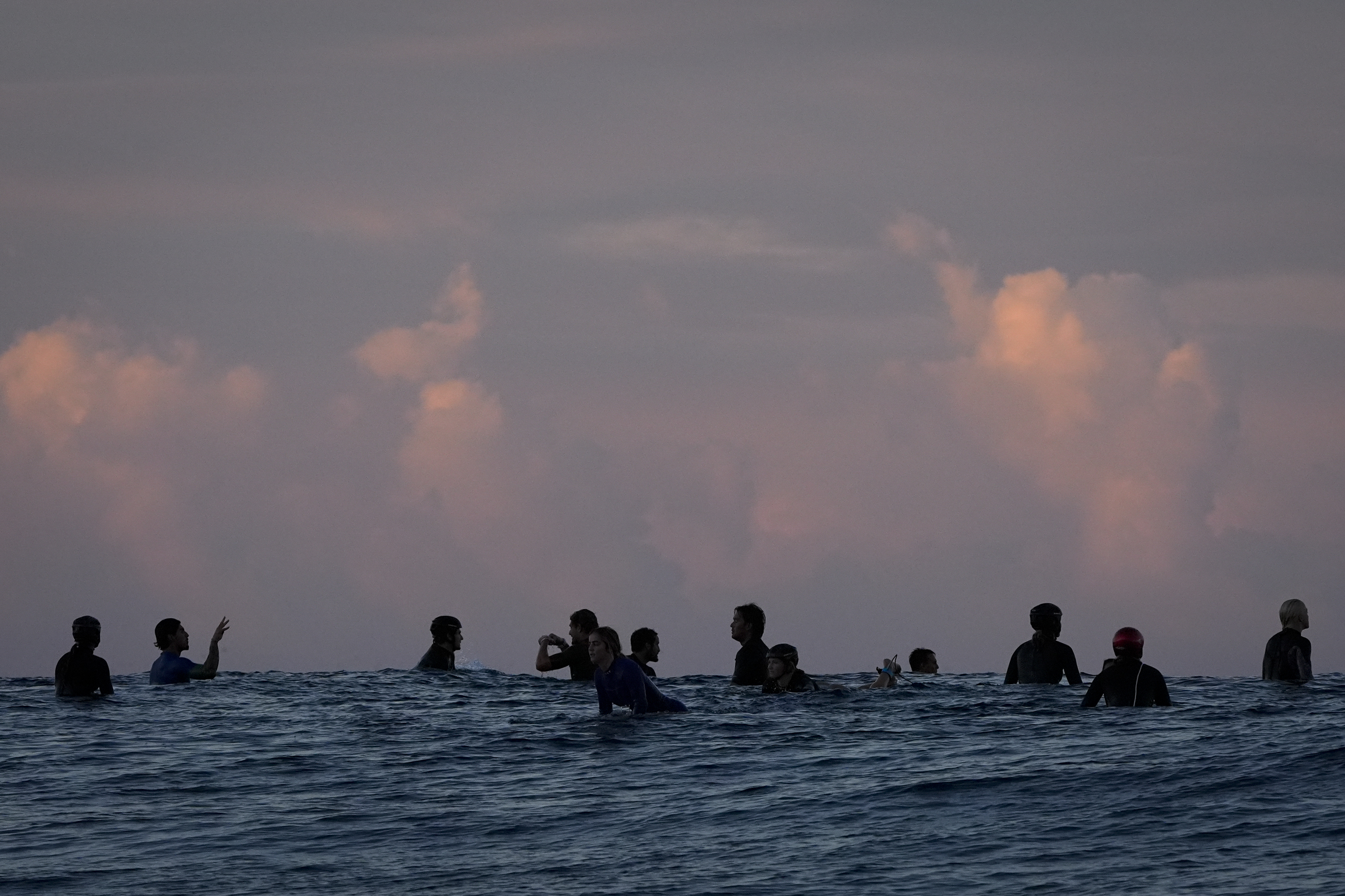 Surfers talk in the lineup before the start of the third round of surfing competition at the 2024 Summer Olympics, Monday, July 29, 2024, in Teahupo'o, Tahiti. 
