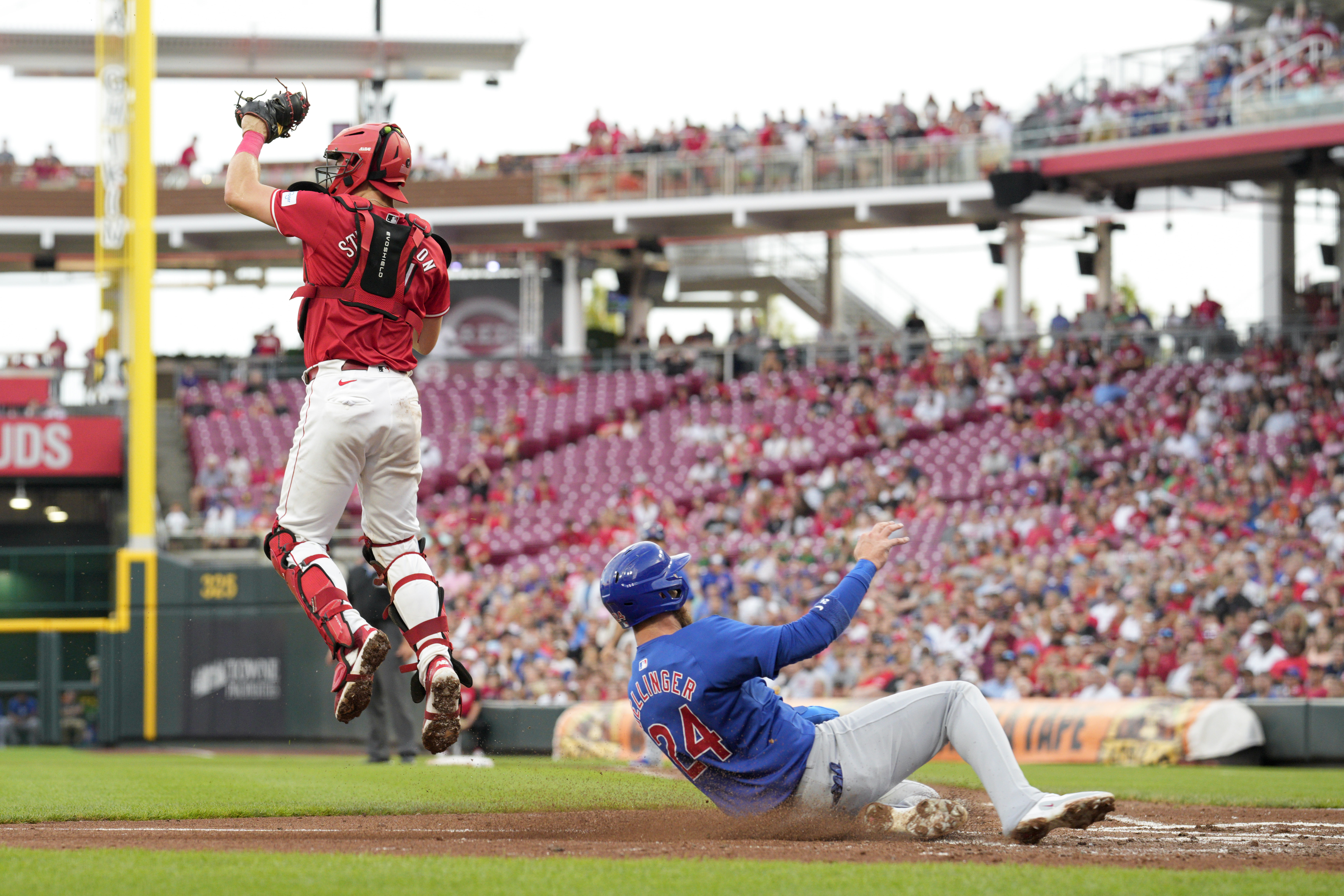 Chicago Cubs' Cody Bollinger (24) scores against Cincinnati Reds catcher Tyler Stephenson on a double hit by teammate Patrick Wisdom during the third inning of a baseball game, Wednesday, July 31, 2024, in Cincinnati.