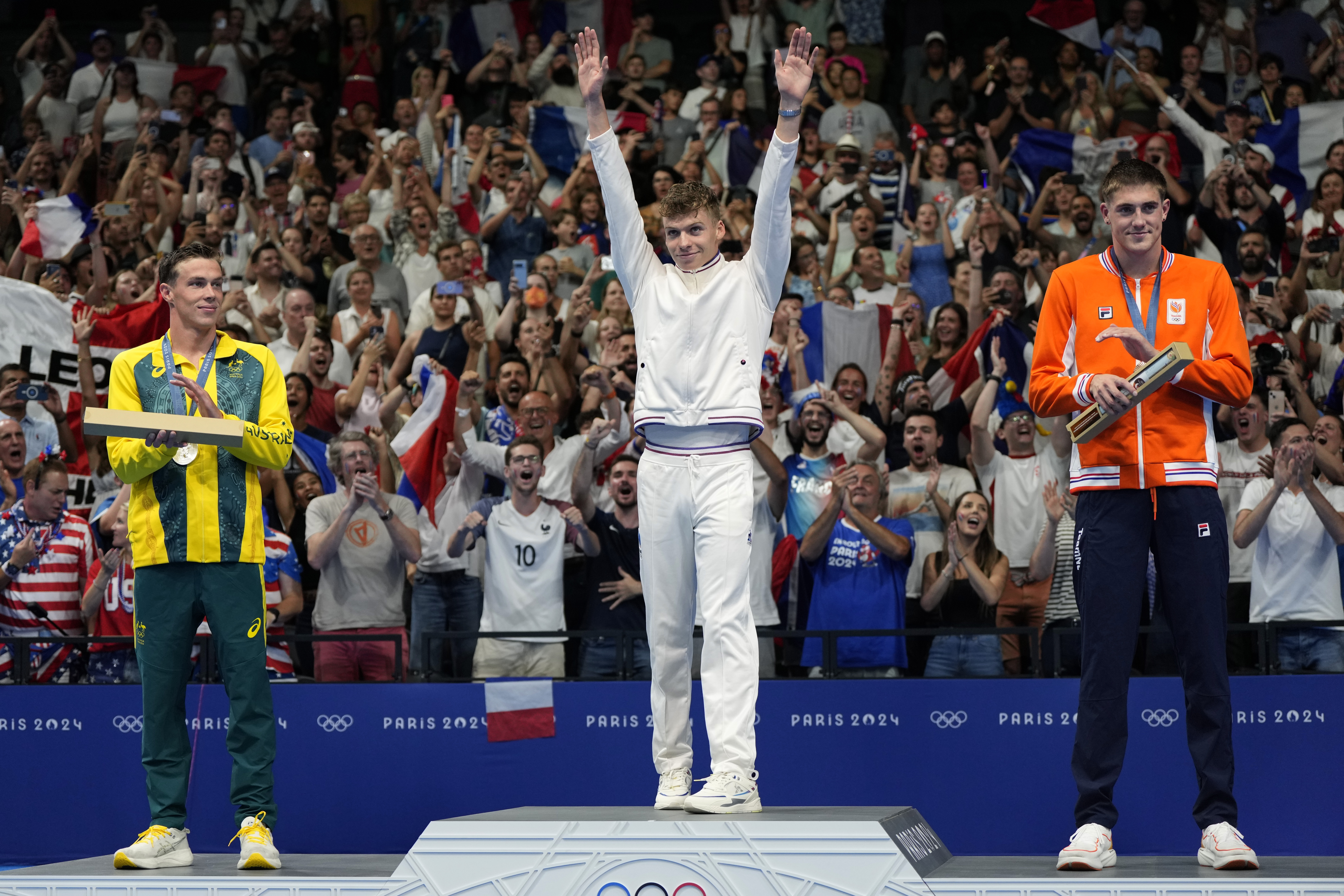 Gold medalist Leon Marchand, center, of France, waves as he stands on the winner's podium with silver medalist Zac Stubblety-Cook, left, of Australia, and bronze medalist Caspar Corbeau, of the Netherlands, following the men's 200-meter breaststroke final at the 2024 Summer Olympics, Wednesday, July 31, 2024, in Nanterre, France. 