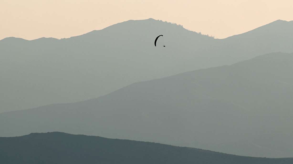 A paraglider moves across the sky in the Salt Lake Valley at sunset on Sunday. The smoky haze is forecast to thin out this weekend as an abnormal high-pressure pattern brings some monsoonal storms.