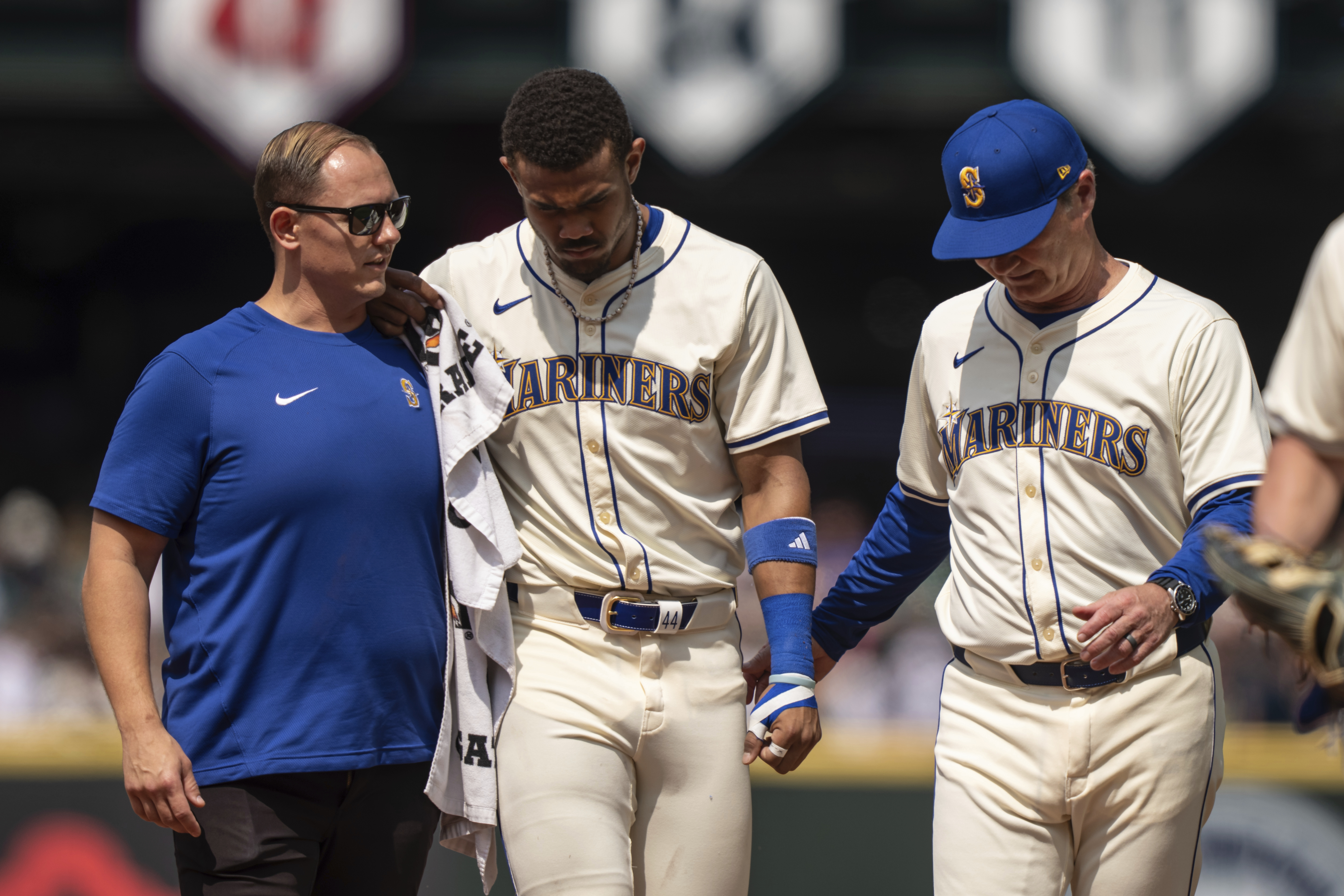 El jardinero central dominicano de los Marineros de Seattle, Julio Rodríguez (centro) es ayudado a salir del campo por el mánager Scott Servais (derecha), y por un integrante del cuerpo técnico durante la sexta entrada del juego de béisbol ante los Astros de Houston, el domingo 21 de julio de 2024, en Seattle. 