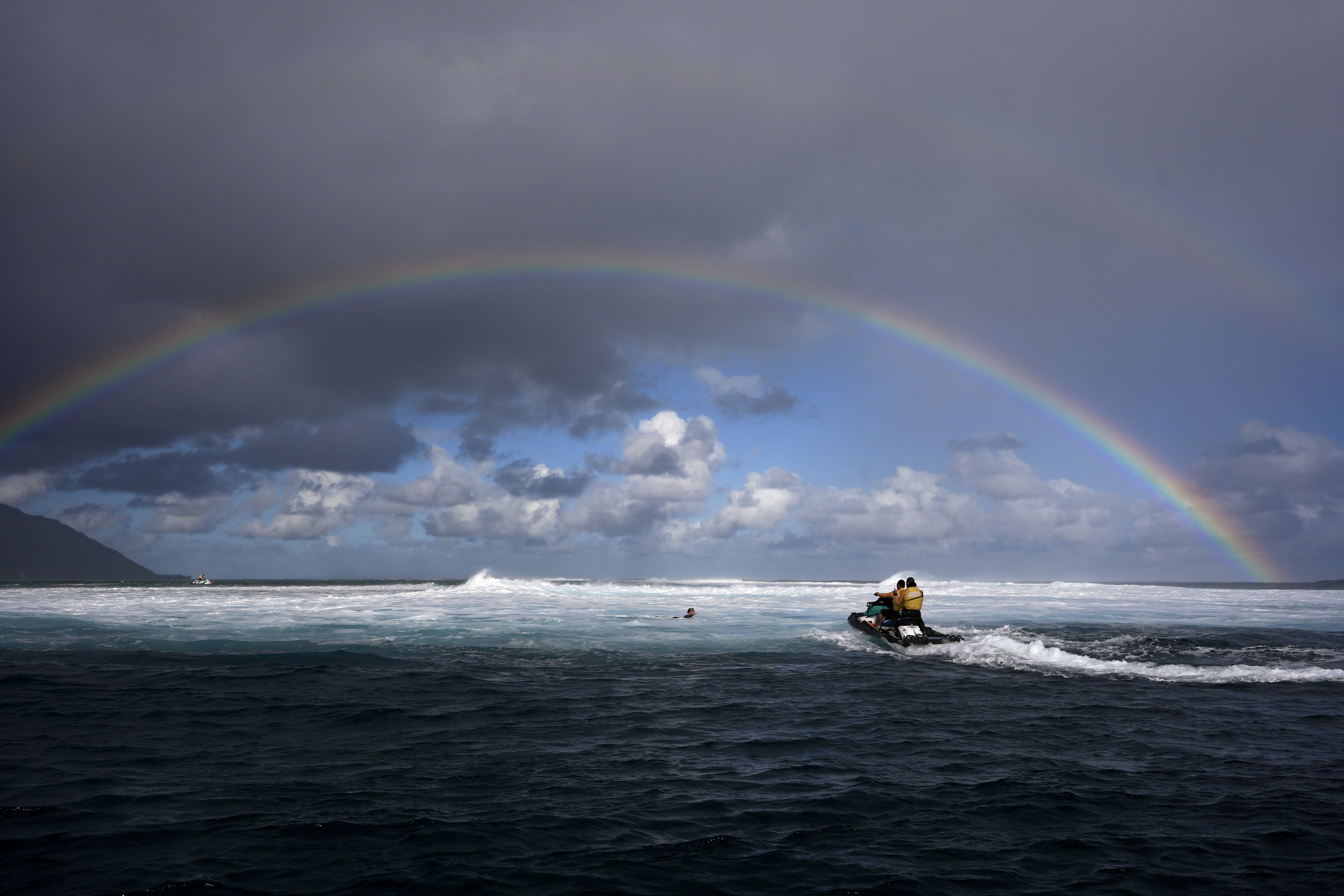 Members of the water safety team move into the impact zone on a jet ski to rescue a surfer under a rainbow during a training day ahead of the 2024 Summer Olympics surfing competition, Tuesday, July 23, 2024, in Teahupo'o, Tahiti. 