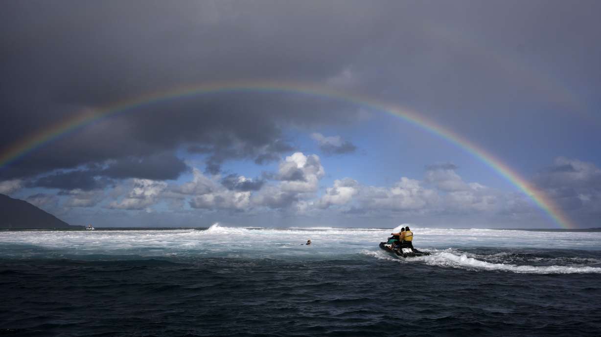 Members of the water safety team move into the impact zone on a jet ski to rescue a surfer under a rainbow during a training day ahead of the 2024 Summer Olympics surfing competition, Tuesday, July 23, 2024, in Teahupo'o, Tahiti.