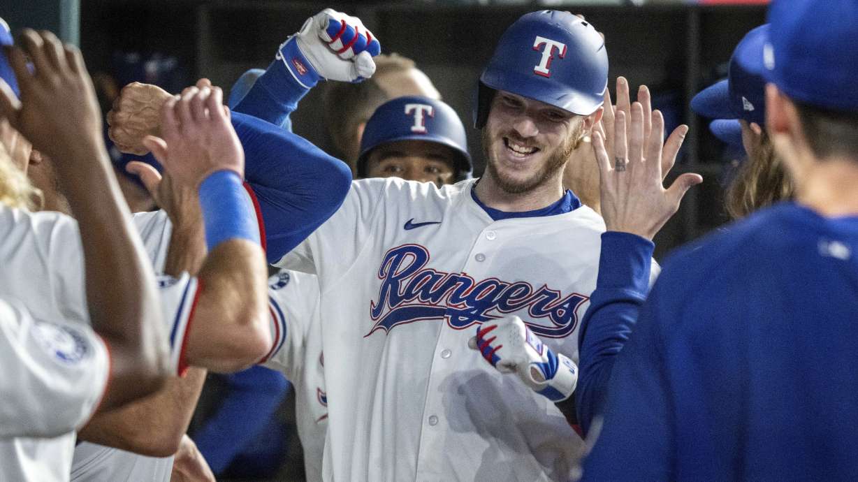 Texas Rangers' Jonah Heim is congratulated in the dugout after hitting a three-run home run off Boston Red Sox starting pitcher Tanner Houck that also scored Ezequiel Duran and Josh Jung during the fourth inning of a baseball game Saturday, Aug. 3, 2024, in Arlington, Texas.