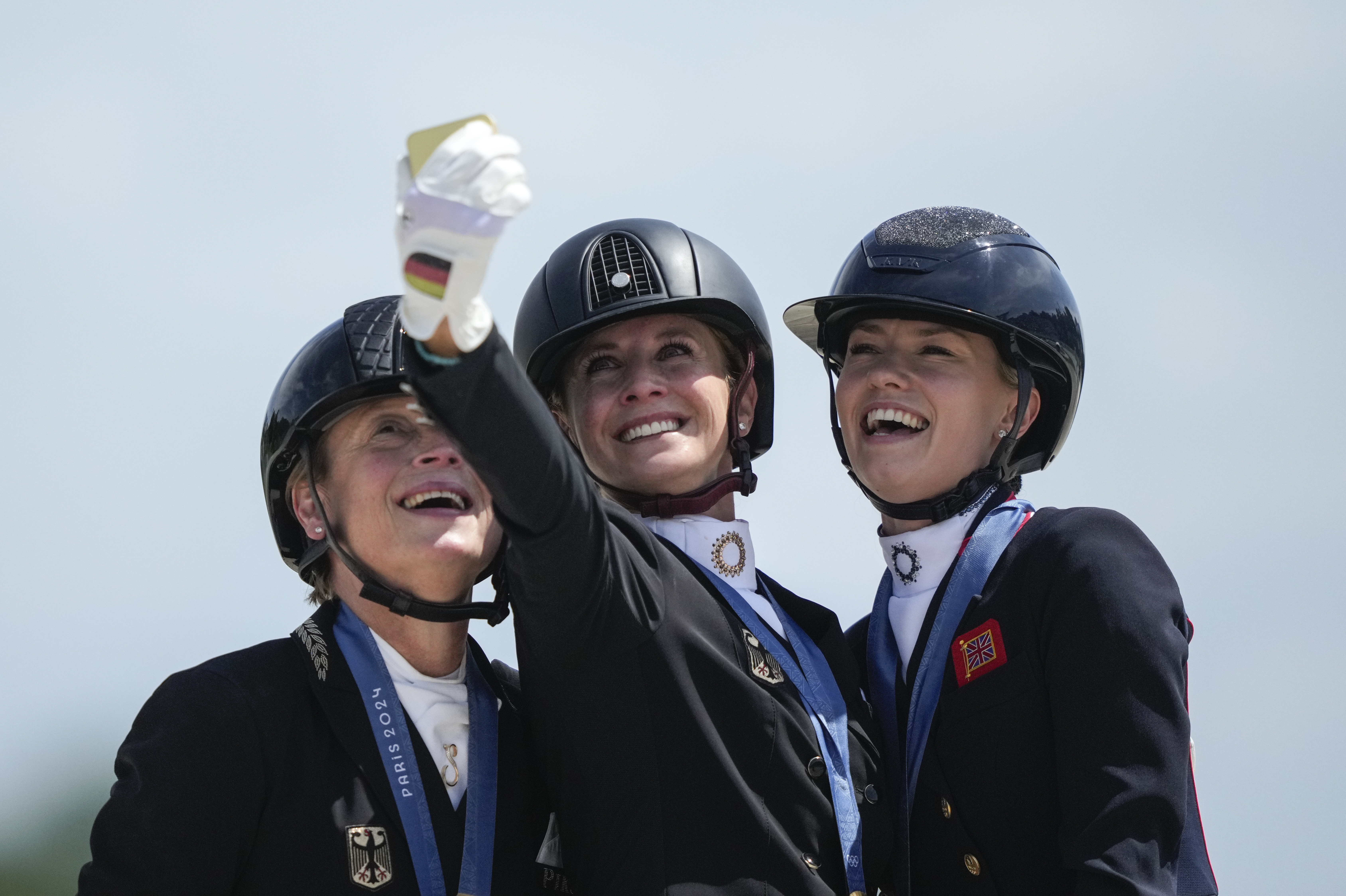 Medalists from left to right, Germany's Isabell Werth, Jessica von Bredow-Werndl and Britain's Charlotte Fry take a selfie to celebrate their silver, gold and bronze medals at the dressage Individual Grand Prix Freestyle, at the 2024 Summer Olympics, Sunday, Aug. 4, 2024, in Versailles, France. 