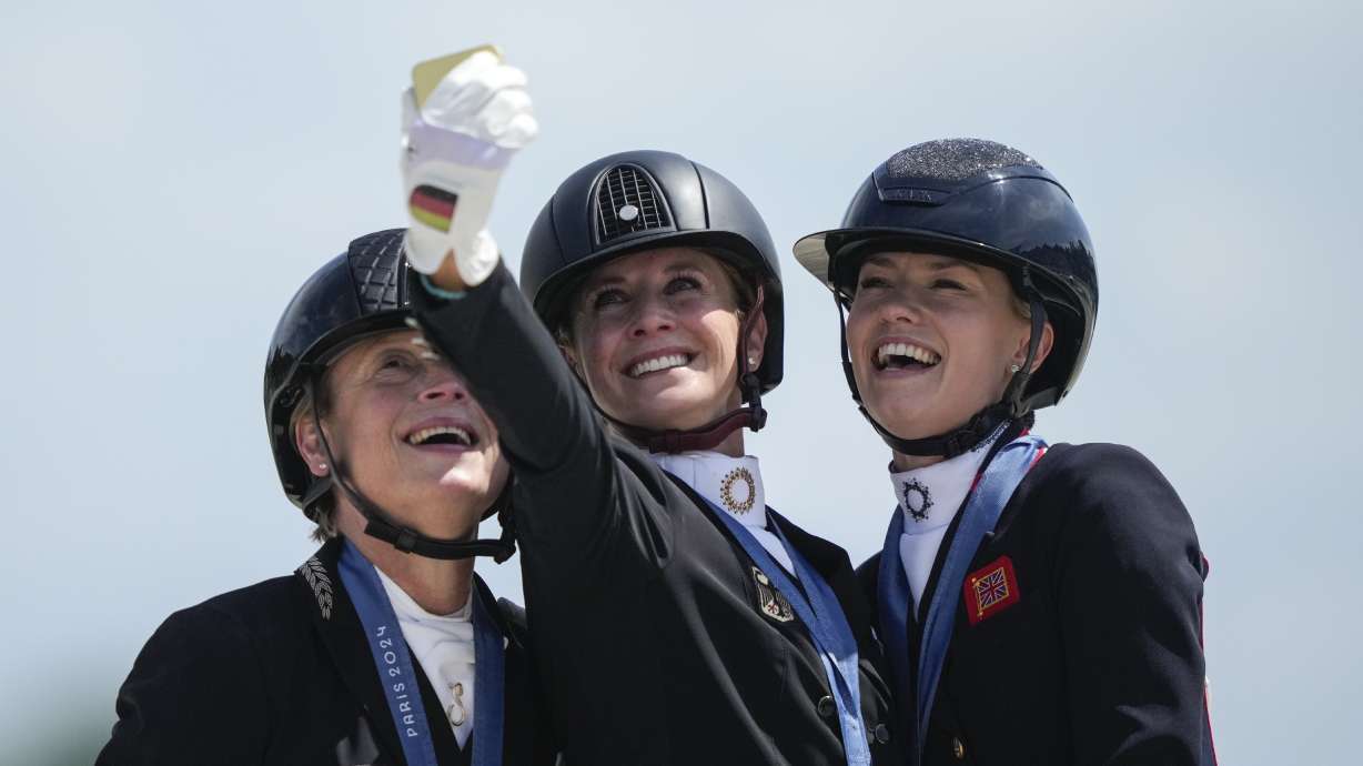 Medalists from left to right, Germany's Isabell Werth, Jessica von Bredow-Werndl and Britain's Charlotte Fry take a selfie to celebrate their silver, gold and bronze medals at the dressage Individual Grand Prix Freestyle, at the 2024 Summer Olympics, Sunday, Aug. 4, 2024, in Versailles, France.