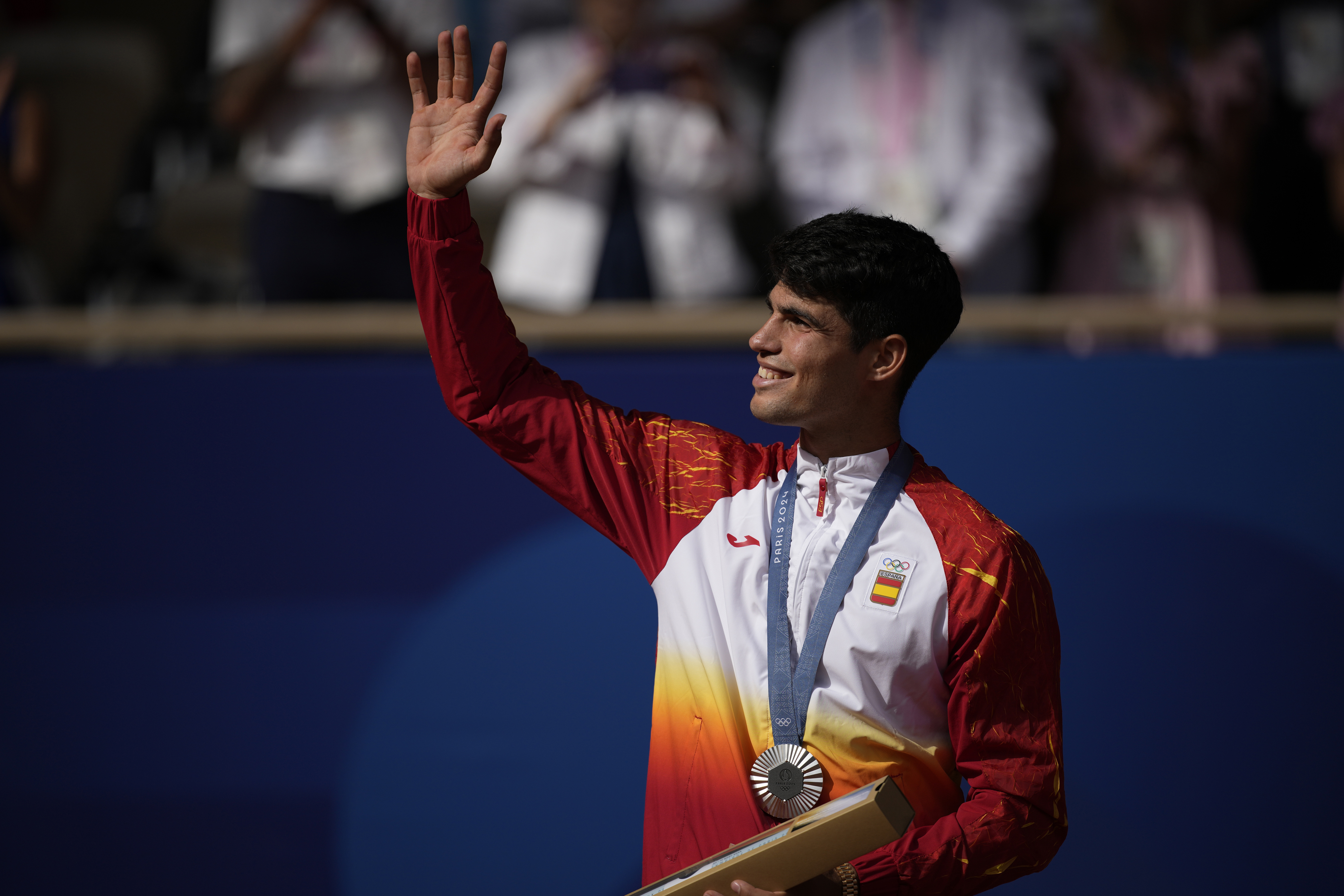 Spain's Carlos Alcaraz waves while wearing his silver medal after losing to Serbia's Novak Djokovic in the men's singles tennis final at the Roland Garros stadium during the 2024 Summer Olympics, Sunday, Aug. 4, 2024, in Paris, France. Djokovic has won his first Olympic gold medal by beating Alcaraz 7-6 (3), 7-6 (2) in the 2024 Games men's tennis singles final. 