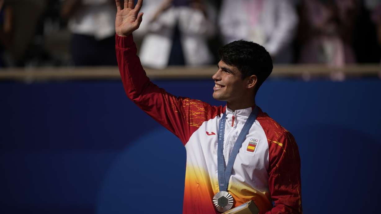 Spain's Carlos Alcaraz waves while wearing his silver medal after losing to Serbia's Novak Djokovic in the men's singles tennis final at the Roland Garros stadium during the 2024 Summer Olympics, Sunday, Aug. 4, 2024, in Paris, France. Djokovic has won his first Olympic gold medal by beating Alcaraz 7-6 (3), 7-6 (2) in the 2024 Games men's tennis singles final.