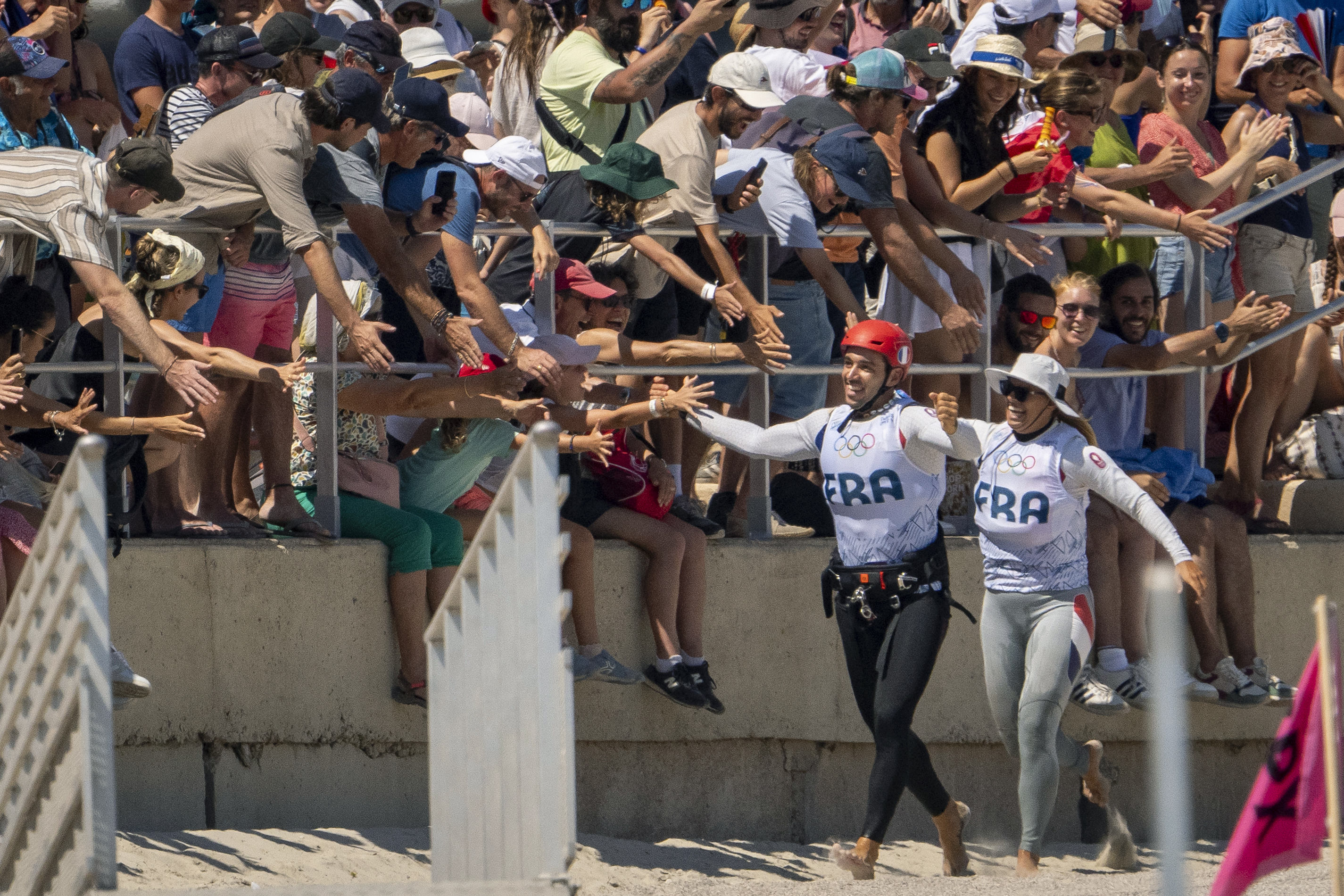 France's Axel Mazella, left, and Lauriane Nolot, high-five fans on the beach just before going out to compete in the men's and women's kite races, Sunday, Aug. 4, 2024, after a delay due to lack of wind, during the 2024 Summer Olympics in Marseille, France.