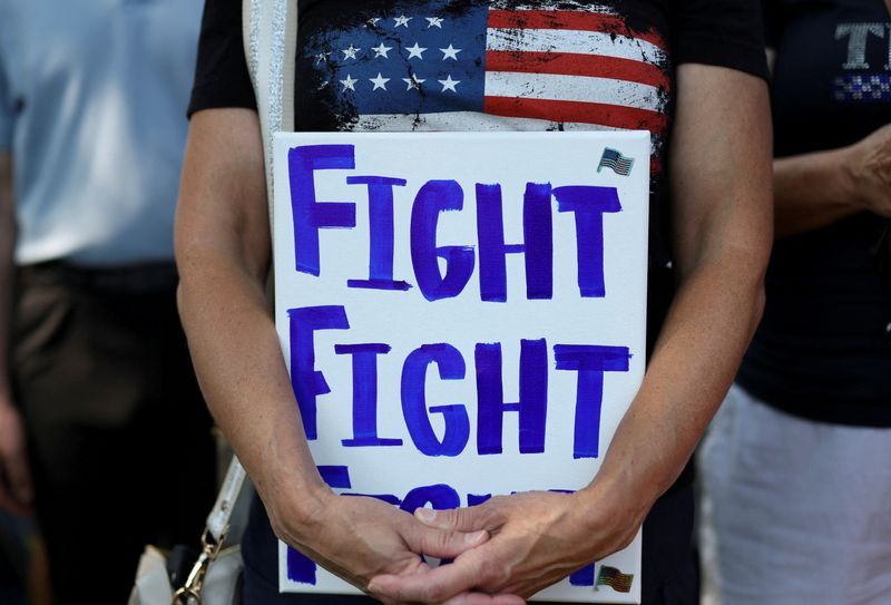 A supporter of former president Donald Trump holds a placard as he and others attend a prayer vigil hosted by Turning Point Action near the venue for the Republican National Convention, at Zeidler Union Square in Milwaukee, Wis., July 14, the day after shots were fired at a Trump rally and he was injured in Butler, Pa.