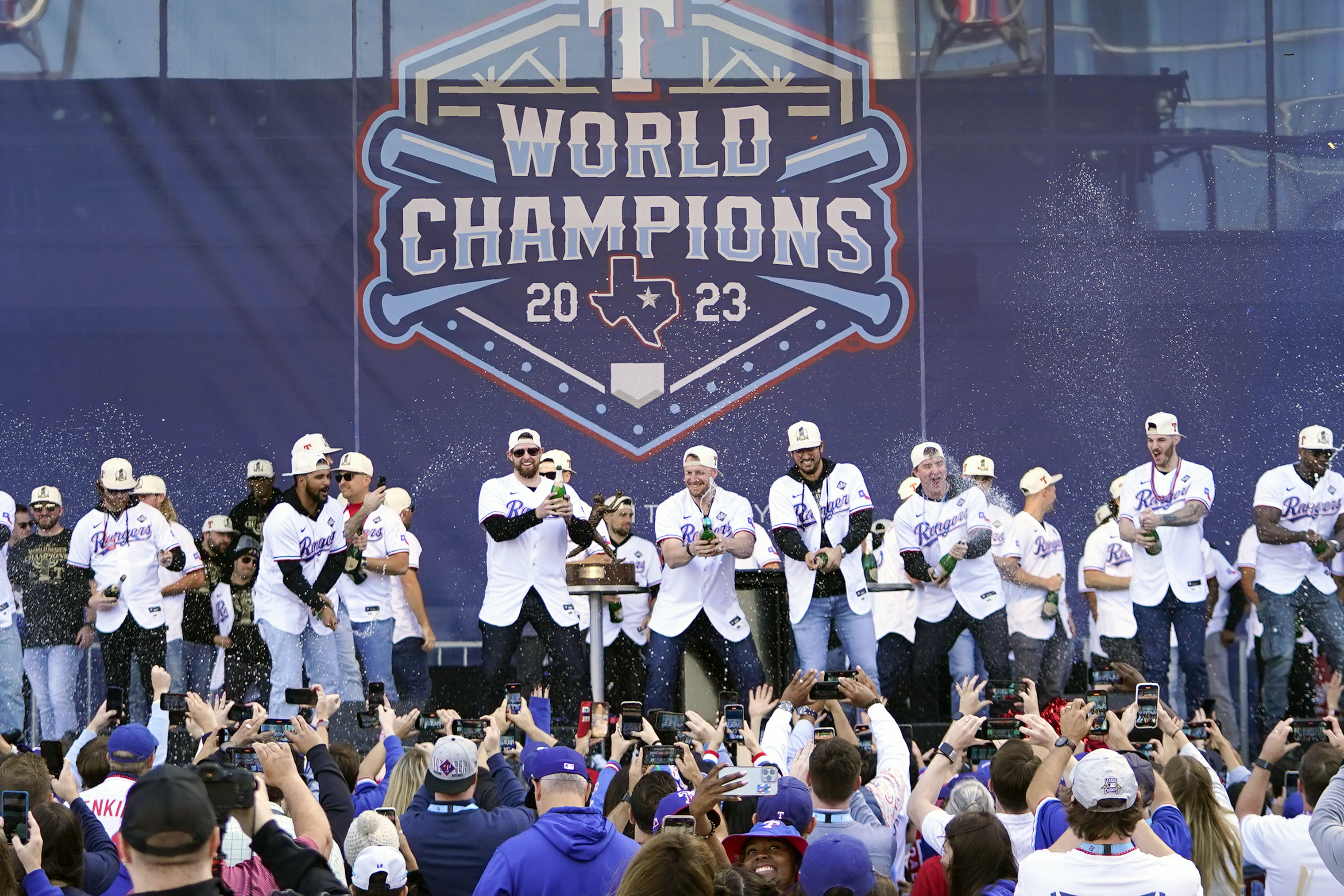 FILE - The Texas Rangers, on stage, spray champagne on fans during a World Series baseball championship celebration, Friday, Nov. 3, 2023, in Arlington, Texas. 