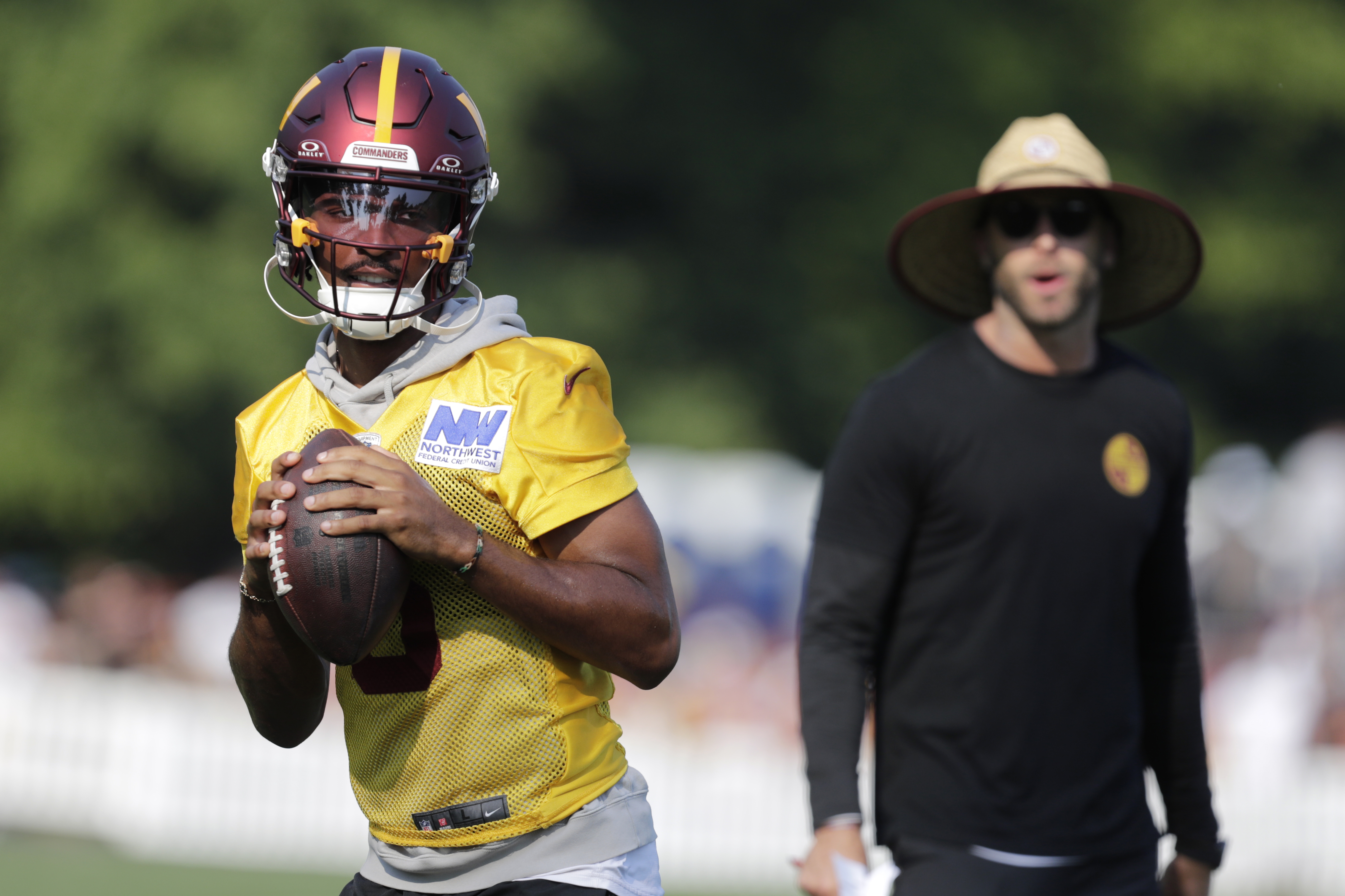 Washington Commanders quarterback Jayden Daniels, left, prepares to pass the ball as offensive coordinator Kliff Kingsbury looks on during an NFL football practice at the team's training facility in Ashburn, Va., Tuesday, Aug. 6, 2024. 