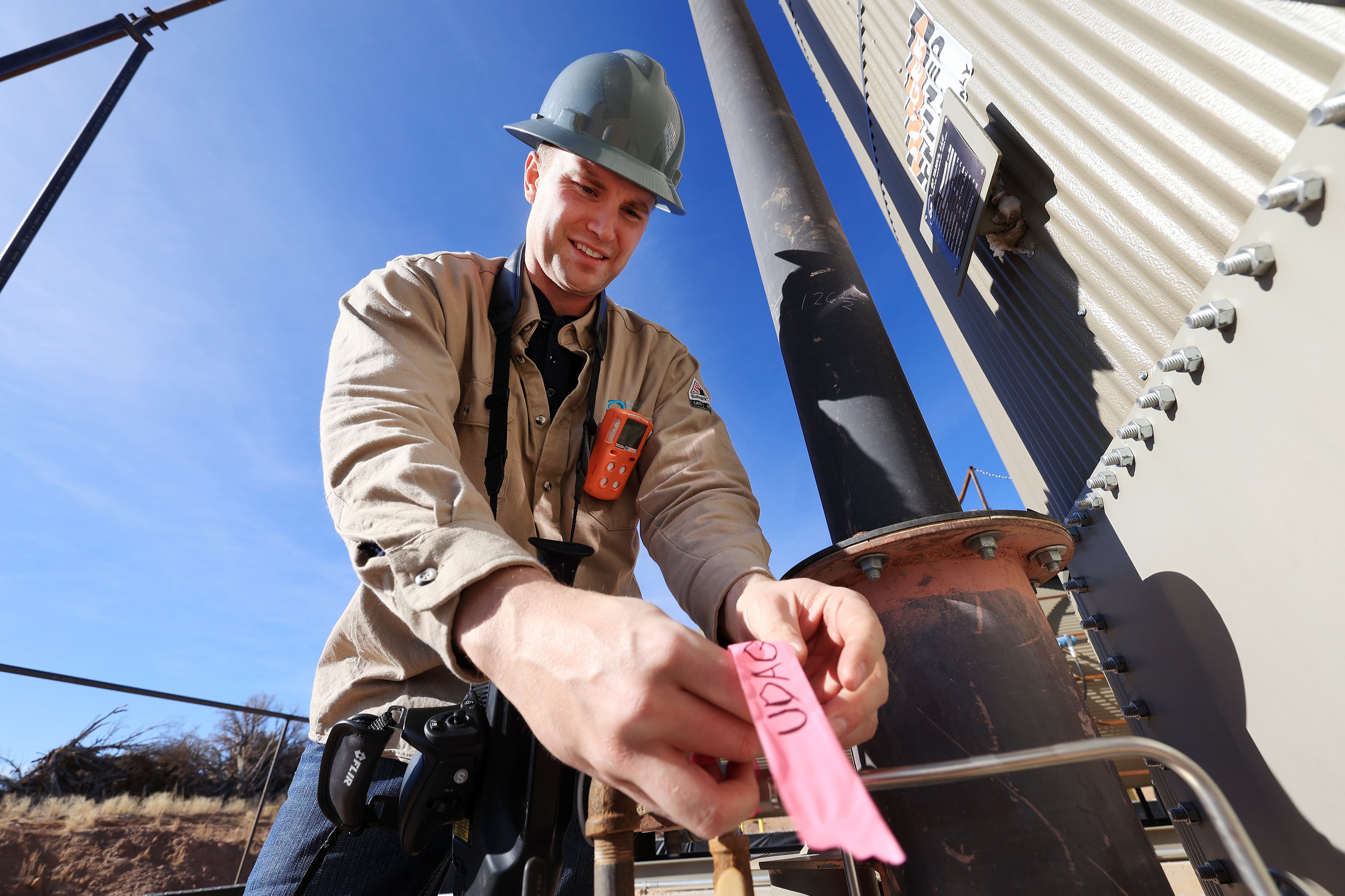 Stephen Foulger, an environmental scientist with the Utah Department of Environmental Quality, ties a pink ribbon around a pipe fitting that has a small gas leak at an oil pump site near Roosevelt on Dec. 1, 2021.