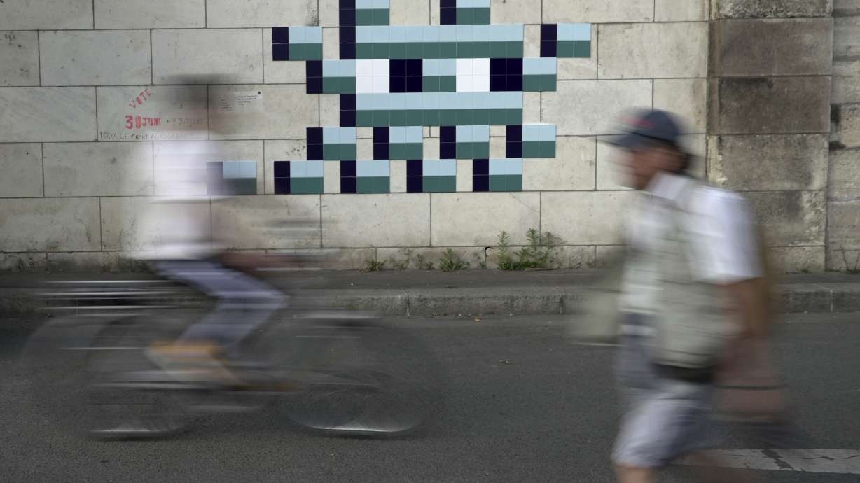 A cyclist rides in front of an Olympic-themed new mosaic by the mysterious French street artist known only by the name Invader, Wednesday Aug. 7, 2024, on the banks of the Seine River, during the 2004 Summer Olympics, in Paris, France.