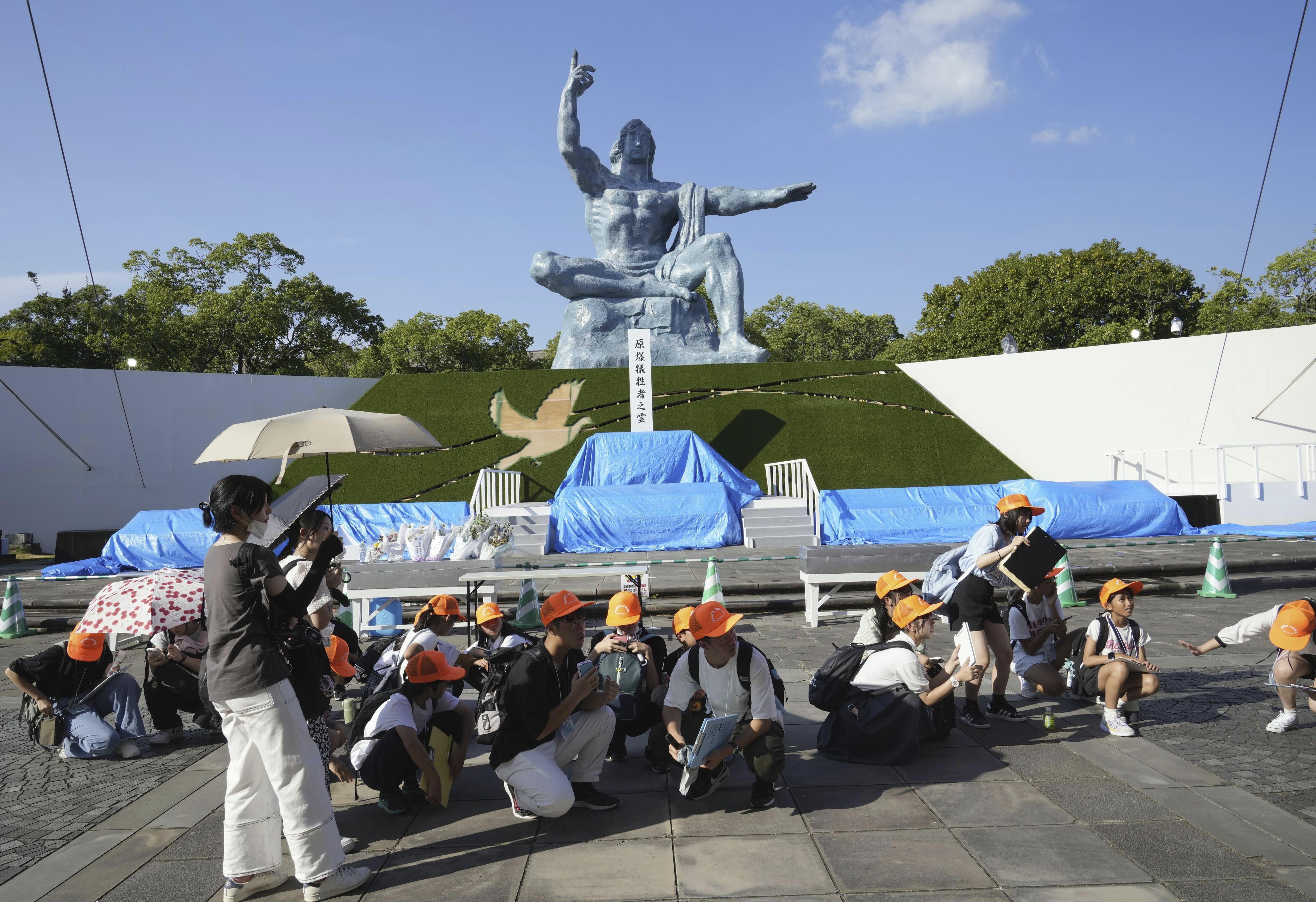Visitors to the Peace Park crouch as an earthquake alert was issued in Nagasaki, western Japan, Thursday.