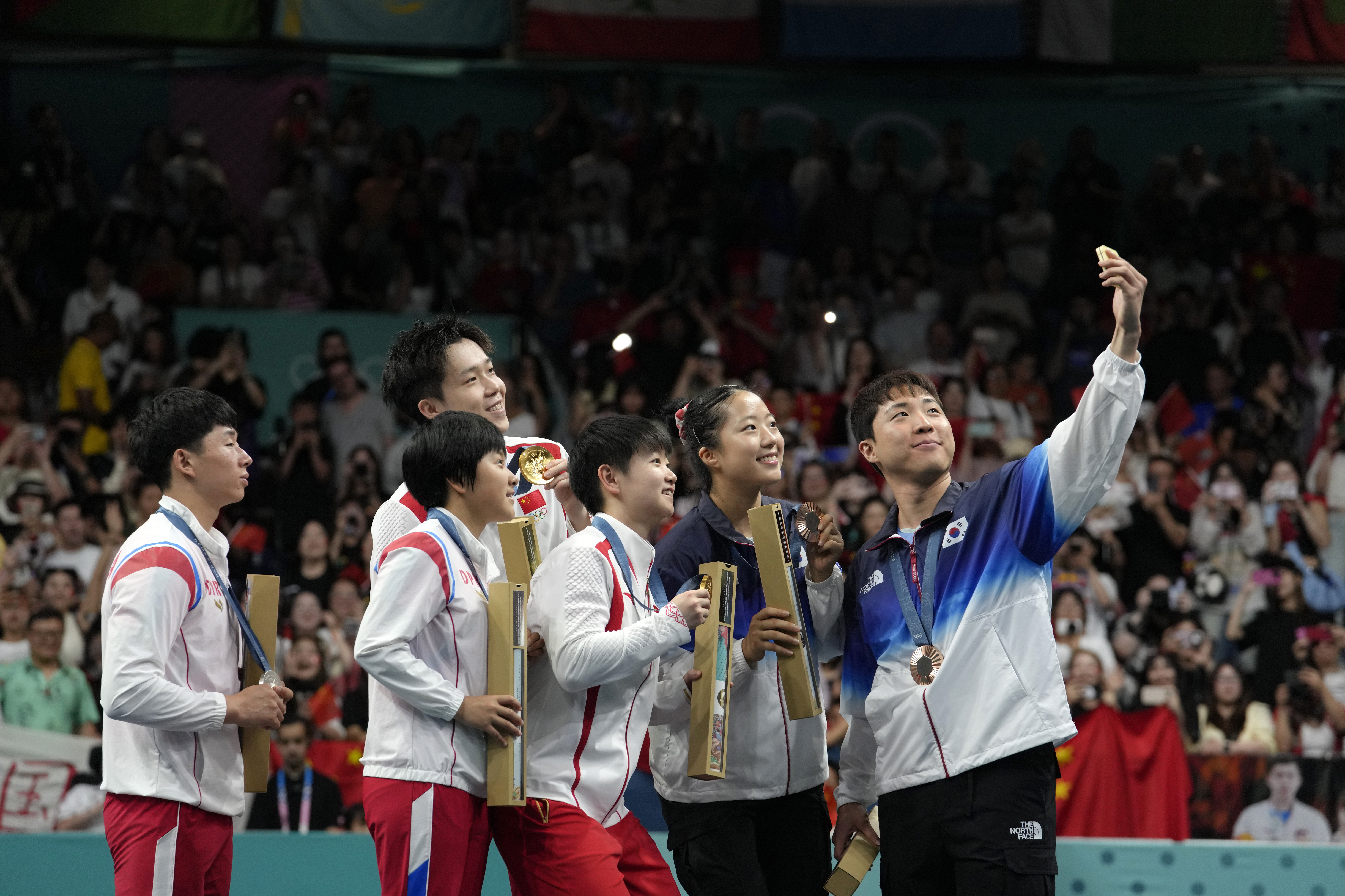 FILE - South Korea's Lim Jonghoon, right, takes a selfie with North Korea's Ri Jong Sik, left, and Kim Kum, second left, China's Wang Chuqin, background, and Sun Yingsha, center, and his teammate Shin Yubin, right, and Lim Jonghoon during the medal ceremony at the 2024 Summer Olympics, July 30, 2024, in Paris, France. 