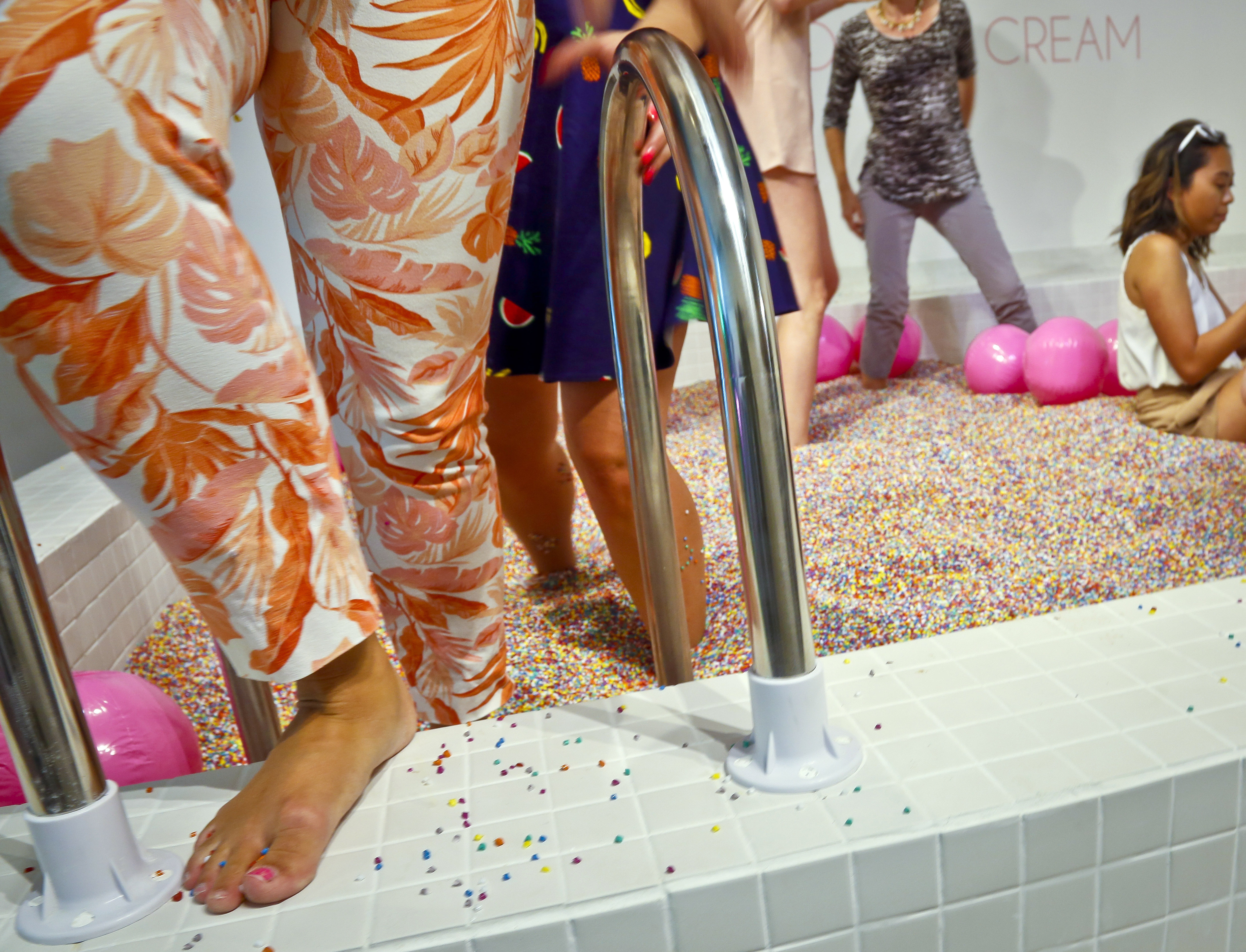 Visitors walk into a large pool filled with faux confetti-colored sprinkles, at the Museum of Ice Cream, July 28, 2016, in New York. A man who says he broke his ankle jumping into the sprinkle pool has filed a lawsuit.