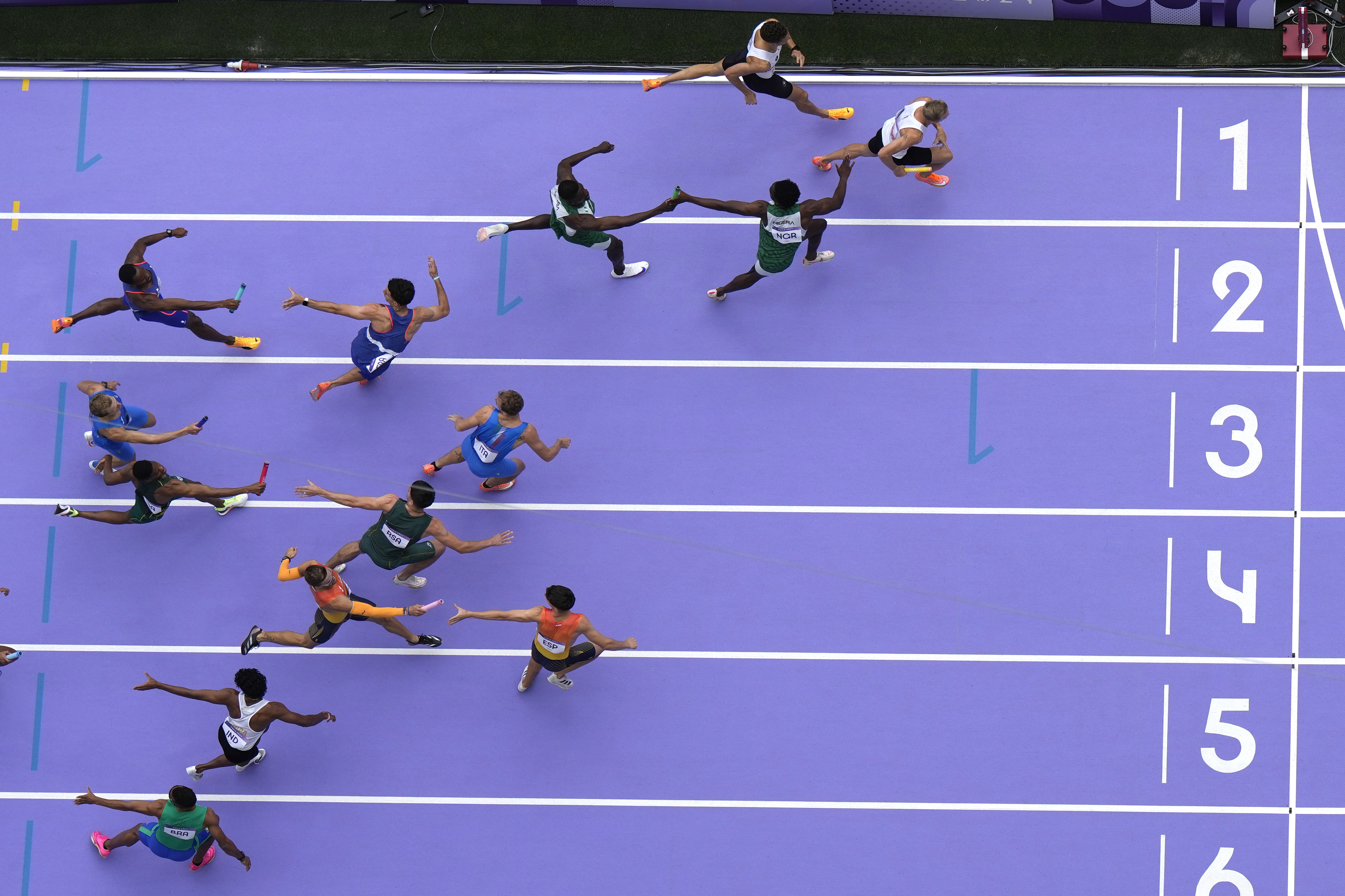 Athletes exchange the baton during a men's 4x400-meter relay heat at the 2024 Summer Olympics, Friday, Aug. 9, 2024, in Saint-Denis, France.