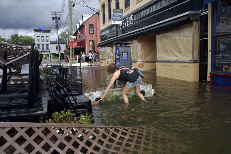 Kari Lynch pick up trash from flood waters near the City Dock in Annapolis, Md., on Friday. First responders launched high-water and helicopter rescues of people trapped in cars and homes along the East coast.