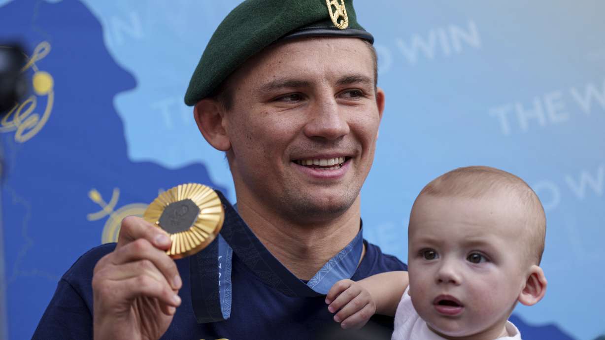 Oleksandr Khyzhniak, Ukraine's Gold medalist of the 2024 Summer Olympics for the men's 80 kg boxing, shows his medal while holding his son Oleksandr after arriving at the train station in Kyiv, Ukraine, Saturday, Aug. 10, 2024.
