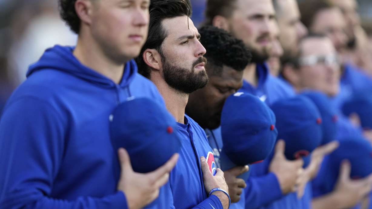 Chicago Cubs shortstop Dansby Swanson, second from left, stands with his hand over his heart during the national anthem before a baseball game against the Chicago White Sox on Saturday, August 10, 2024, in Chicago. The Cubs' shortstop went from a bundle of nerves to unbridled joy as he watched alone on a couch in his basement. His wife Mallory scored the lone goal in a 1-0 win over Brazil to propel the Americans to their fifth gold medal.