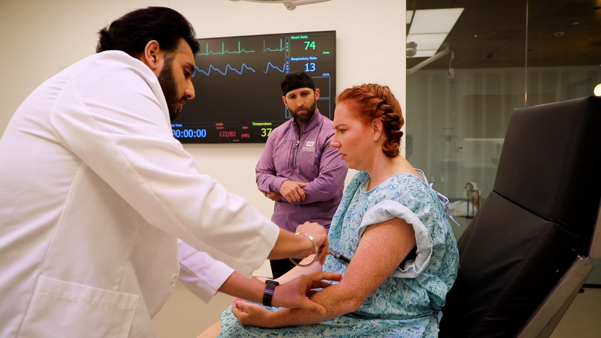 A simulation operating room is pictured with Parminder Deo, a second year medical student, and Whitney Hall, a Standardized Patient, while Adam Jennings observes at the Burnett School of Medicine, Texas Christian University.