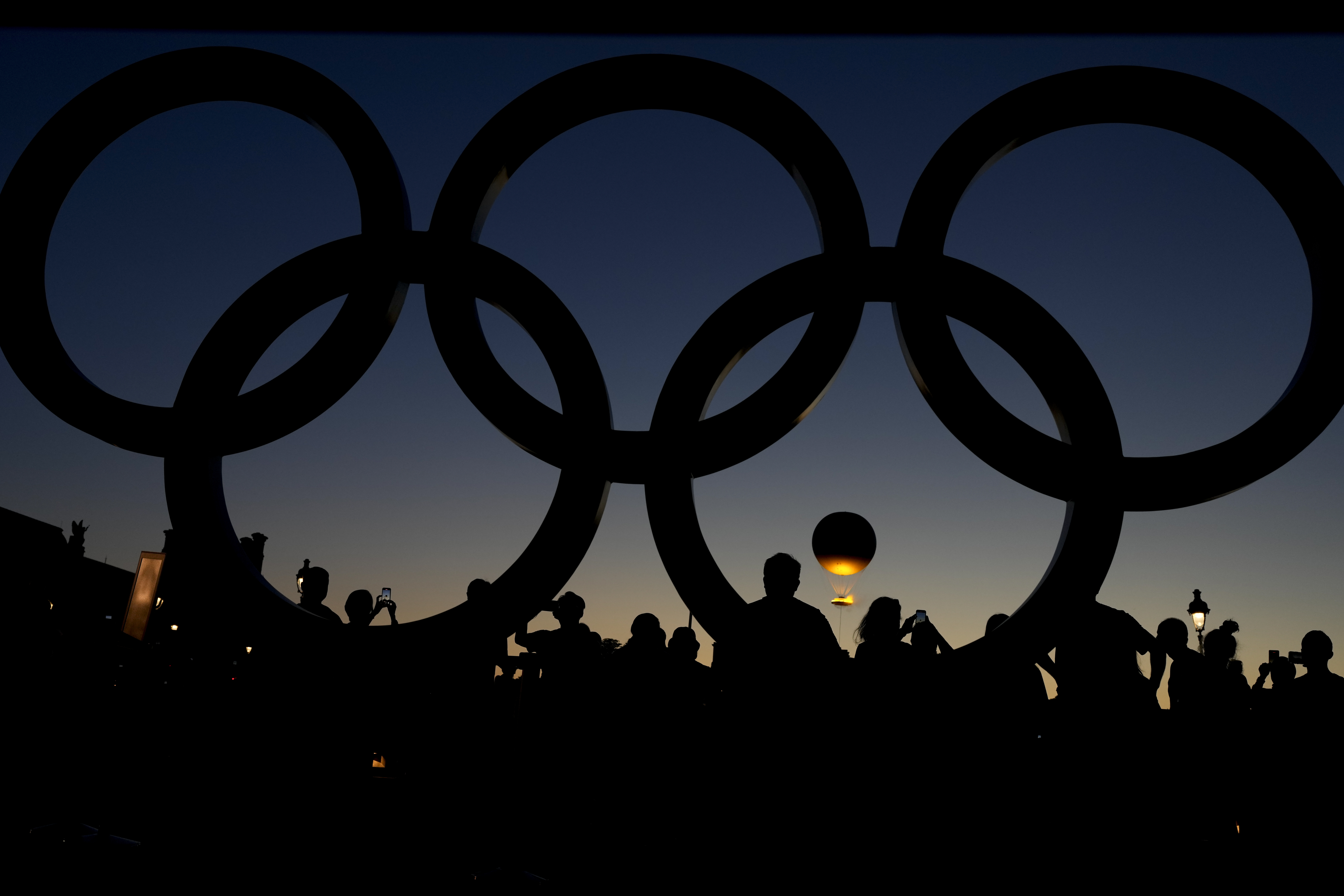 People watch the cauldron rise at sunset by the Olympic rings during the 2024 Summer Olympics, Monday, Aug. 5, 2024, in Paris, France.