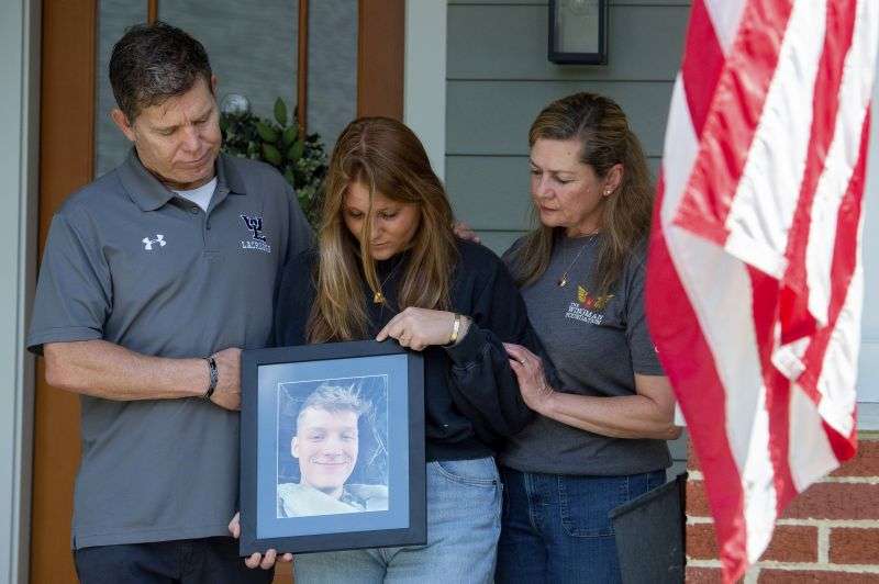 Family members of Marine Cpl. Spencer R. Collart, from left, father Bart Collart, sister Gwyneth Collart and mother Alexia Collart, hold his portrait as they pose for a photo at their home in Arlington, Va., June 19.
