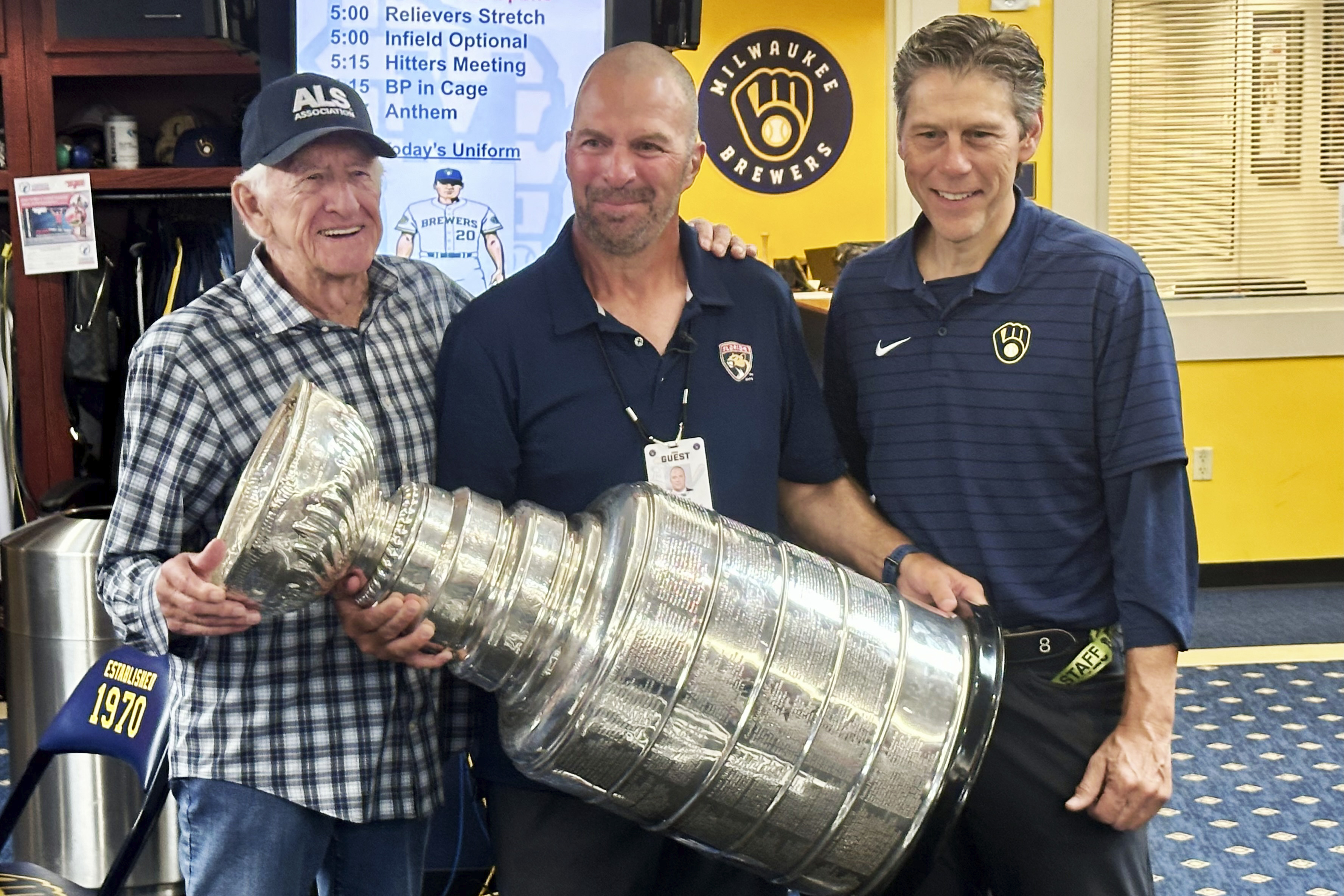 Longtime Milwaukee Brewers broadcaster Bob Uecker, left, Florida Panthers general manager Bill Zito, and Brewers director of clubhouse operations Tony Migliaccio pose with the Stanley Cup in the team's clubhouse before a baseball game against the Los Angeles Dodgers, Wednesday, Aug. 14, 2024, in Milwaukee. 