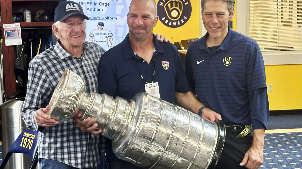 Longtime Milwaukee Brewers broadcaster Bob Uecker, left, Florida Panthers general manager Bill Zito, and Brewers director of clubhouse operations Tony Migliaccio pose with the Stanley Cup in the team's clubhouse before a baseball game against the Los Angeles Dodgers, Wednesday, Aug. 14, 2024, in Milwaukee.