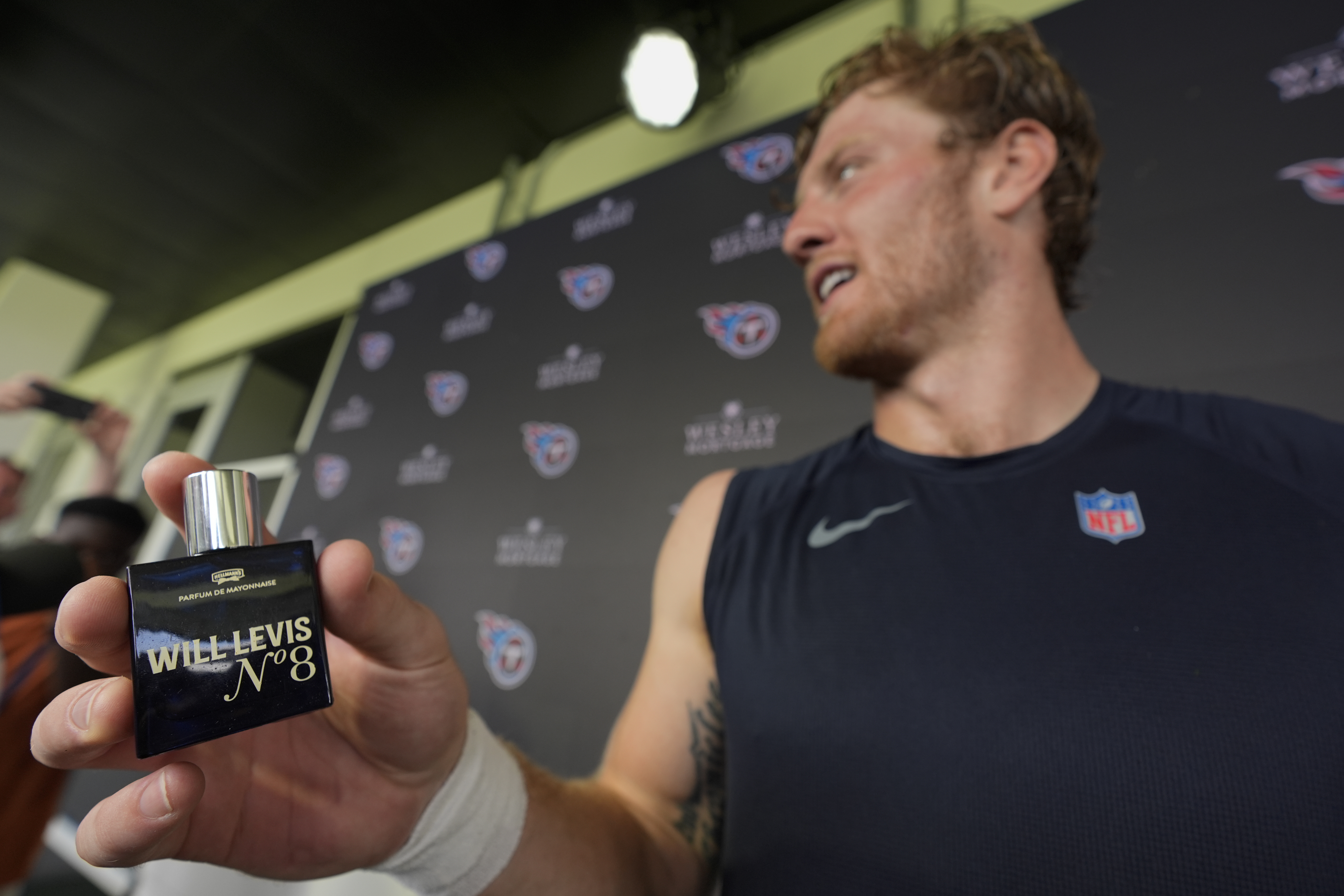 Tennessee Titans quarterback Will Levis, right, holds a bottle of his new cologne after a news conference following an NFL joint football training camp practice with the Seattle Seahawks, Wednesday, Aug. 14, 2024, in Nashville, Tenn.