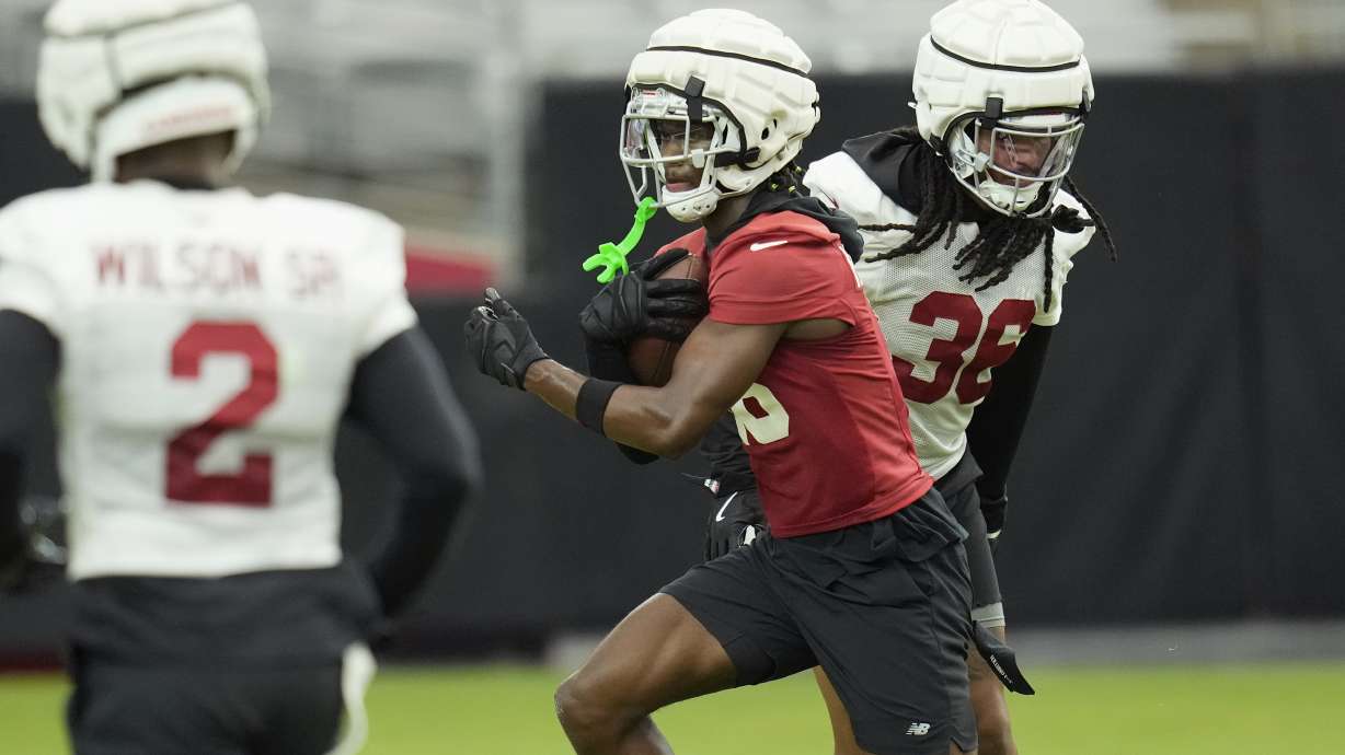 Arizona Cardinals wide receiver Marvin Harrison Jr., center, makes a catch between Cardinals linebacker Mack Wilson Sr. (2) and Cardinals safety Andre Chachere (36) as players take part in drills during an NFL football training camp at the State Farm Stadium Thursday, Aug. 1, 2024, in Glendale, Ariz.