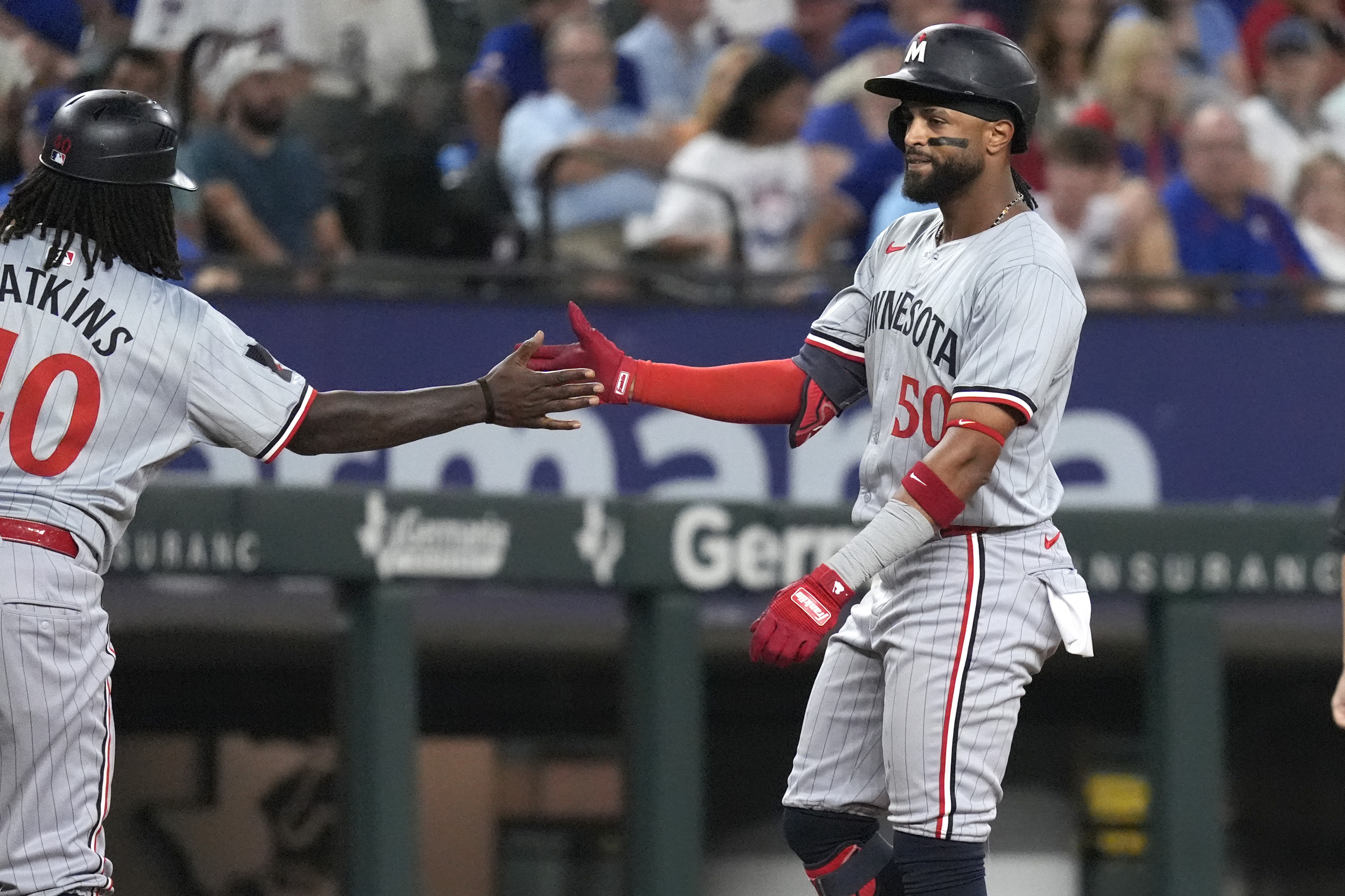Minnesota Twins' Willi Castro, right, gets a congratulatory hand from third base coach Tommy Watkins, left, after singling to score teammates Edouard Julien and Christian Vázquez during the eighth inning of a baseball game against the Texas Rangers in Arlington, Texas, Saturday, Aug. 17, 2024. Castro reached third base on a throwing error by Rangers center fielder Leody Taveras.