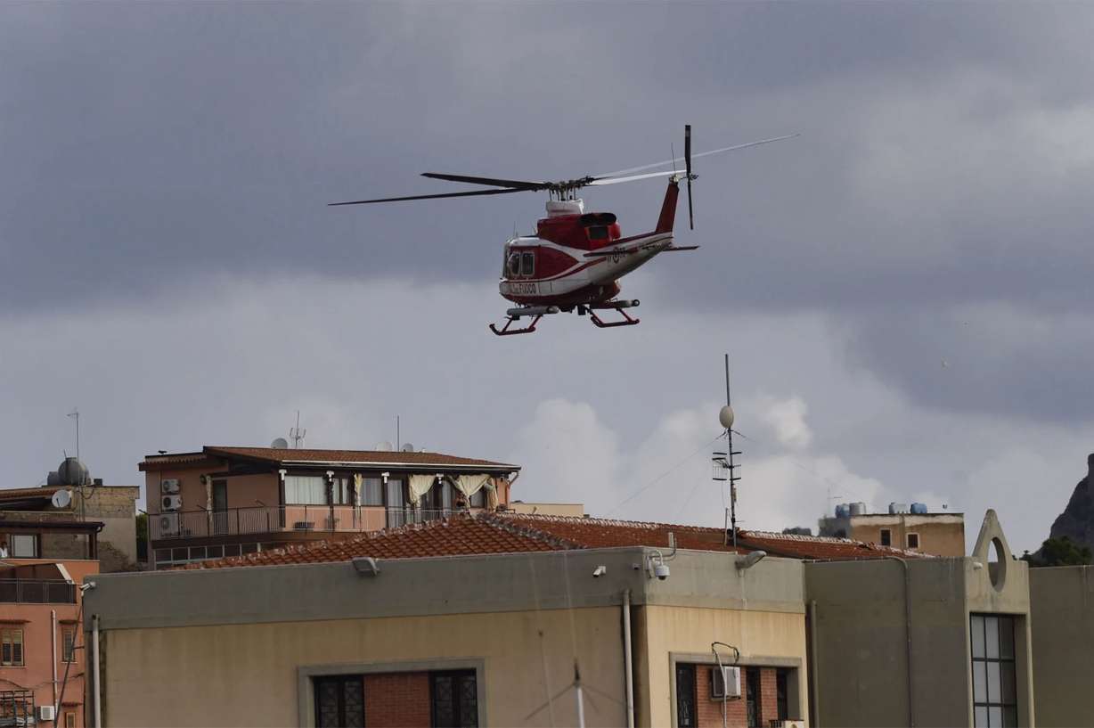 An Italian firefighters helicopter flies over houses near the harbor of Porticello, southern Italy, Tuesday, as rescue teams and divers returned to the site of a storm-sunken yacht to search for six people, including British tech magnate Mike Lynch, who are believed to be still trapped in the hull 164-feet underwater.