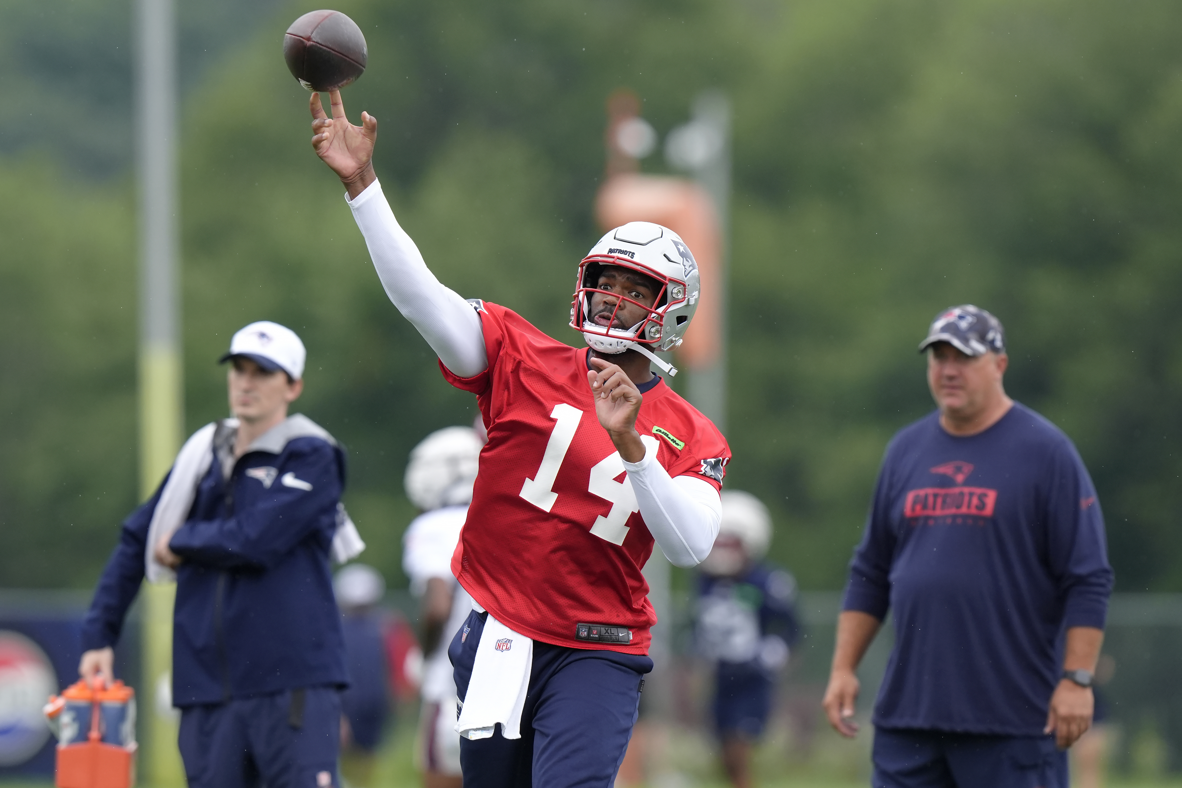 New England Patriots quarterback Jacoby Brissett (14) passes the ball in front of offensive coordinator Alex Van Pelt, right, during an NFL football training camp, Wednesday, July 24, 2024, in Foxborough, Mass. 