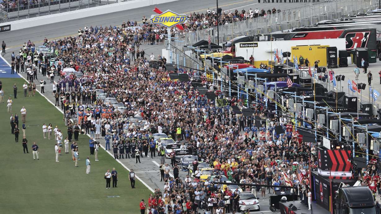 Drivers, crew members and guests stand on pit road for the national anthem before a NASCAR Cup Series auto race at Daytona International Speedway, Saturday, Aug. 24, 2024, in Daytona Beach, Fla.