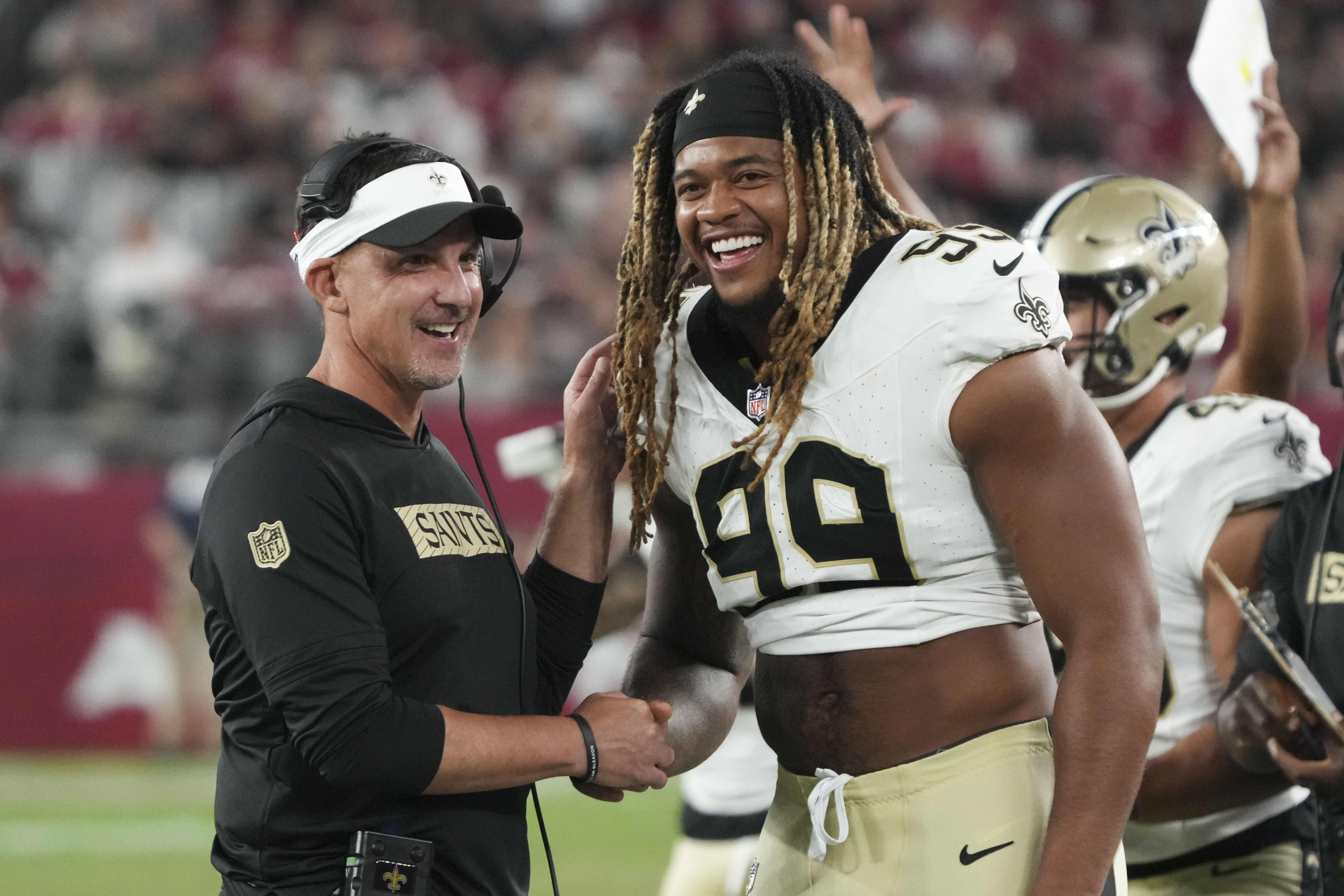 New Orleans Saints head coach Dennis Allen laughs with defensive end Chase Young (99) in the second half of a preseason NFL football game against the Arizona Cardinals, Saturday, Aug. 10, 2024, in Glendale, Ariz. 