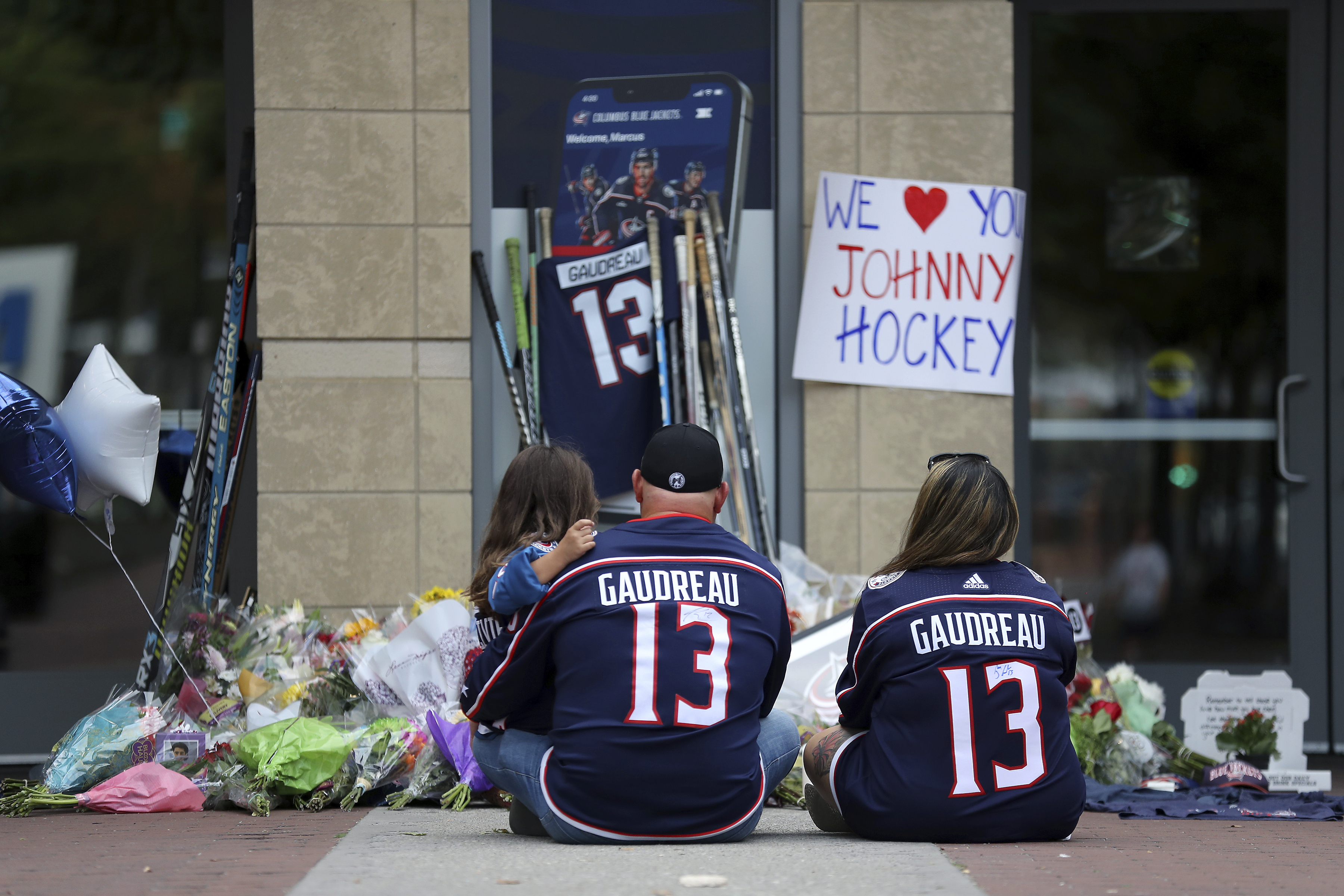 Shiloh Rivera, left, mourns with Hylas Stemen, center, and Amanda Rivera of Columbus, at the makeshift memorial set up by fans for Blue Jackets hockey player Johnny Gaudreau in Columbus, Ohio, Aug. 30, 2024. Gaudreau, along with his brother Matthew, was fatally struck by a motorist while riding his bicycle on Thursday.