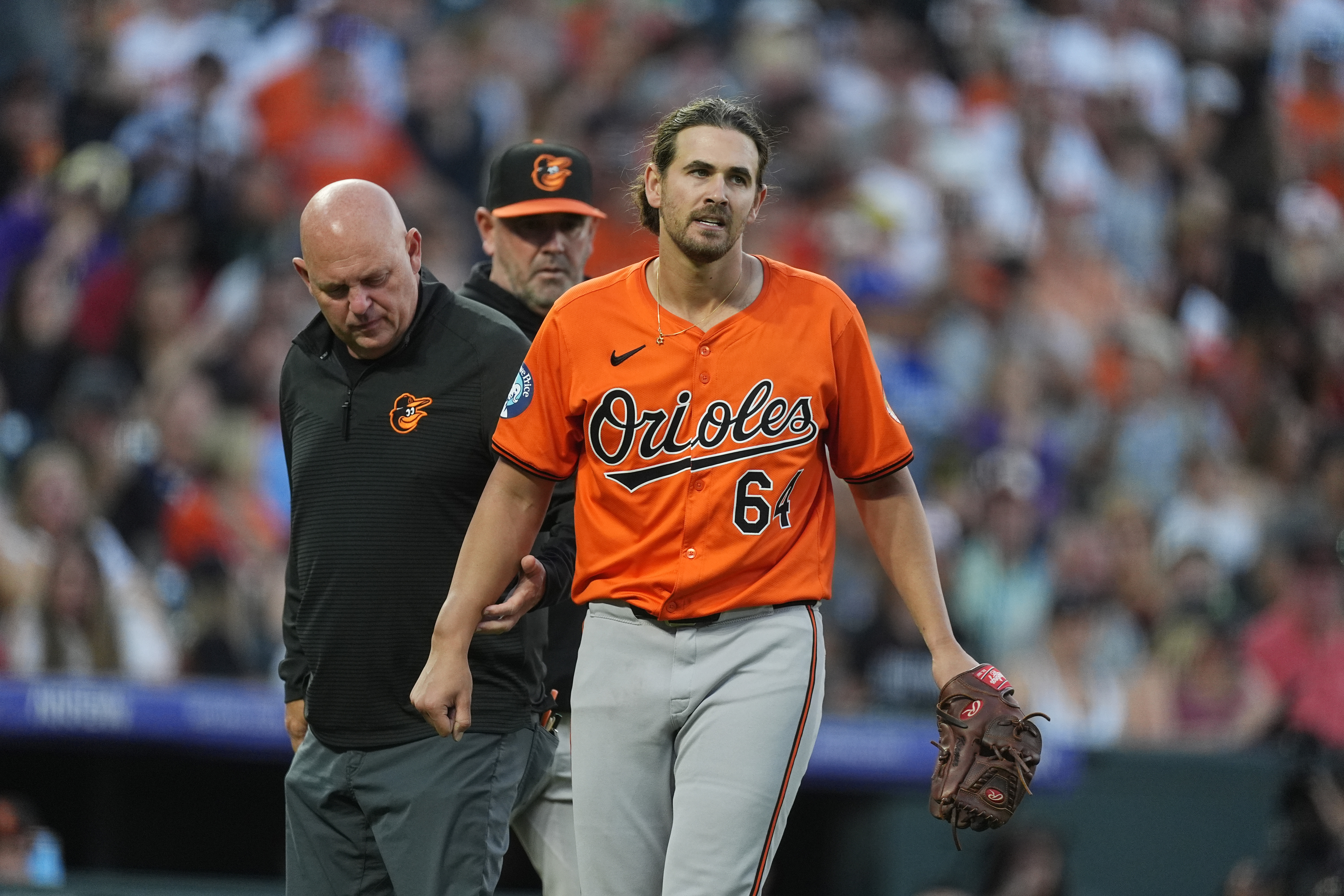 A trainer, left, checks the arm of Baltimore Orioles starting pitcher Dean Kremer, right, after Kremer was hit by a ground ball off the bat of Colorado Rockies' Jordan Beck in the fourth inning of a baseball game Saturday, Aug. 31, 2024, in Denver. Orioles manager Brandon Hyde, center, looks on. 