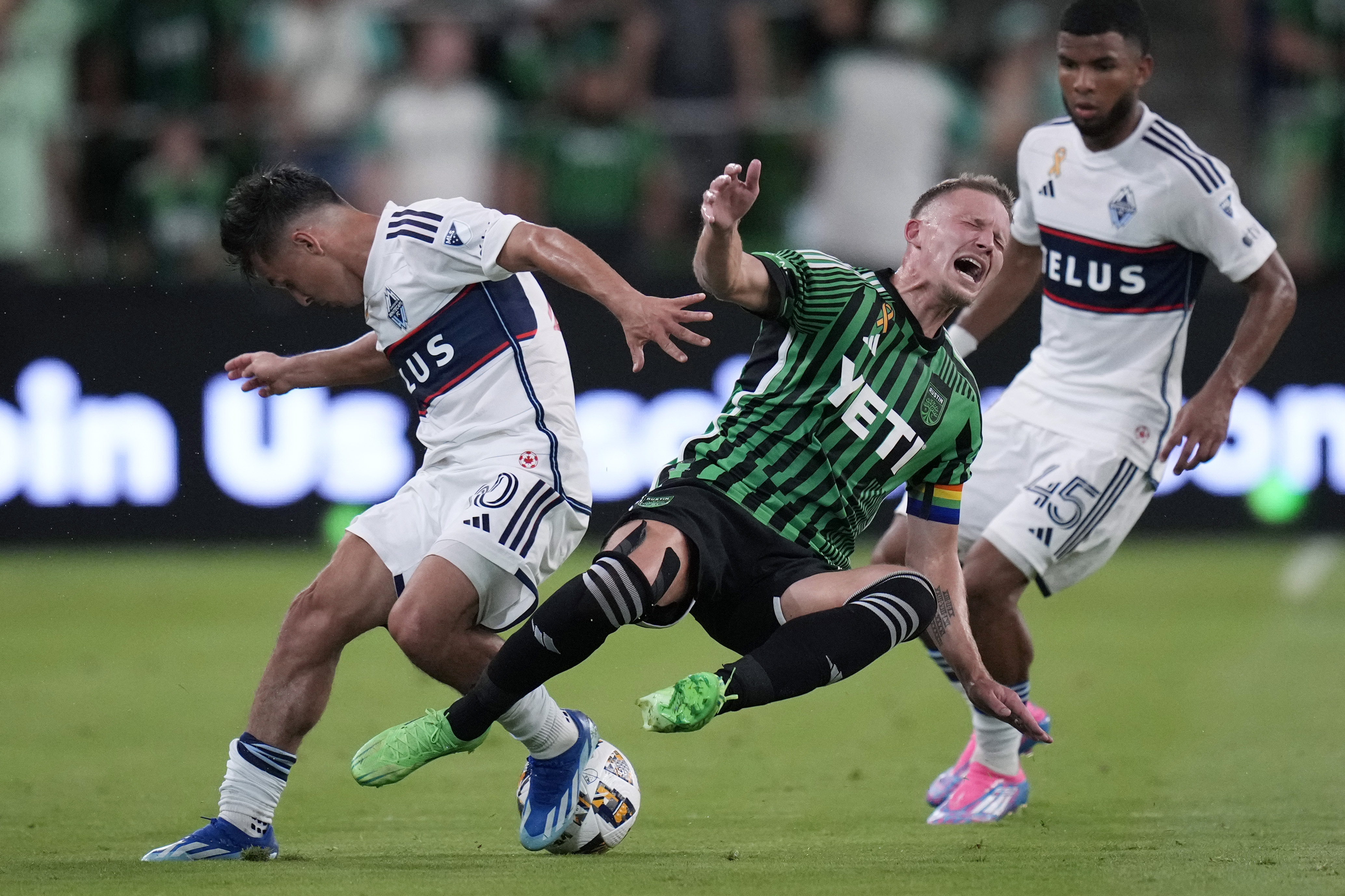 Austin FC midfielder Alexander Ring, center, is tripped as he and Vancouver Whitecaps midfielder Andres Cubas, left, compete for the ball during the first half of an MLS soccer match in Austin, Texas, Saturday, Aug. 31, 2024. 