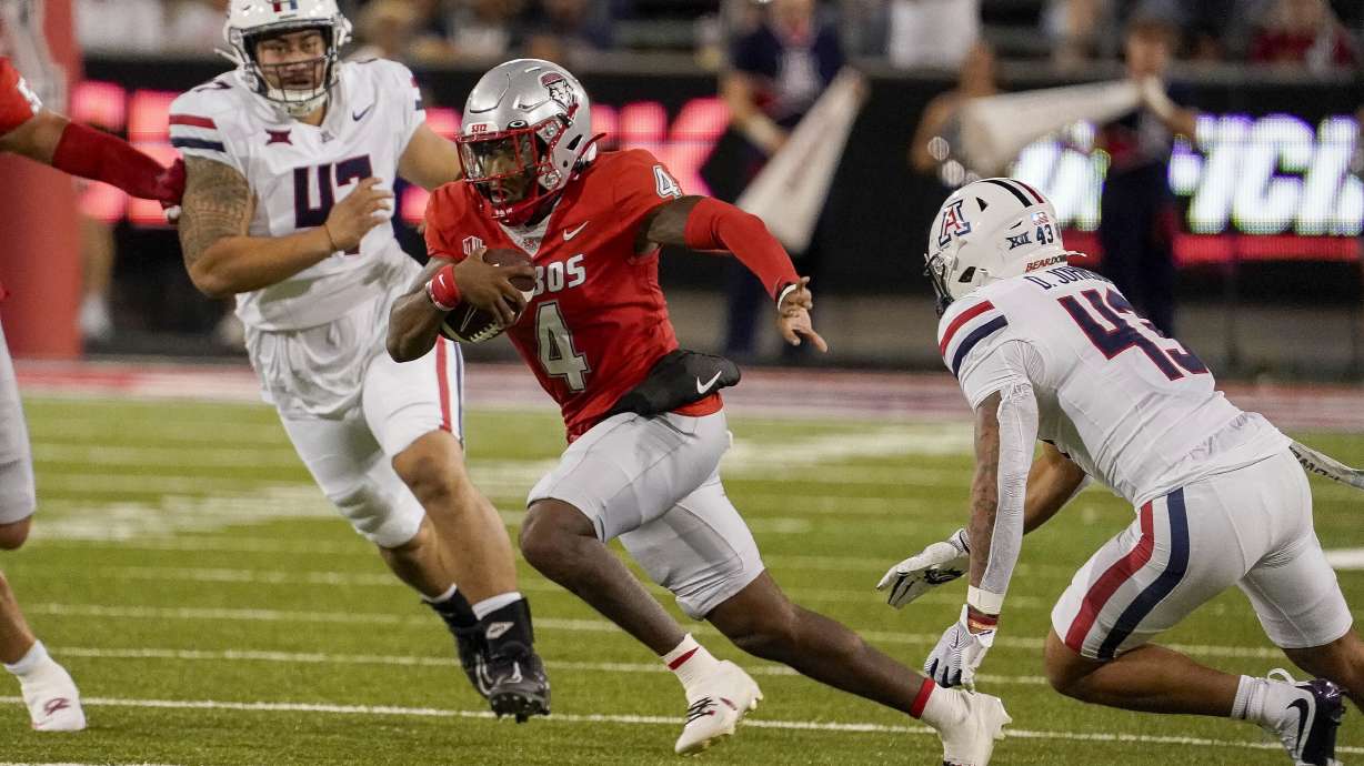New Mexico quarterback Devon Dampier (4) scrambles for a first down against Arizona's Stanley Ta'ufo'ou, left and Dalton Johnson, right, during the first half of an NCAA college football game Saturday, Aug 31, 2024, in Tucson, Ariz.