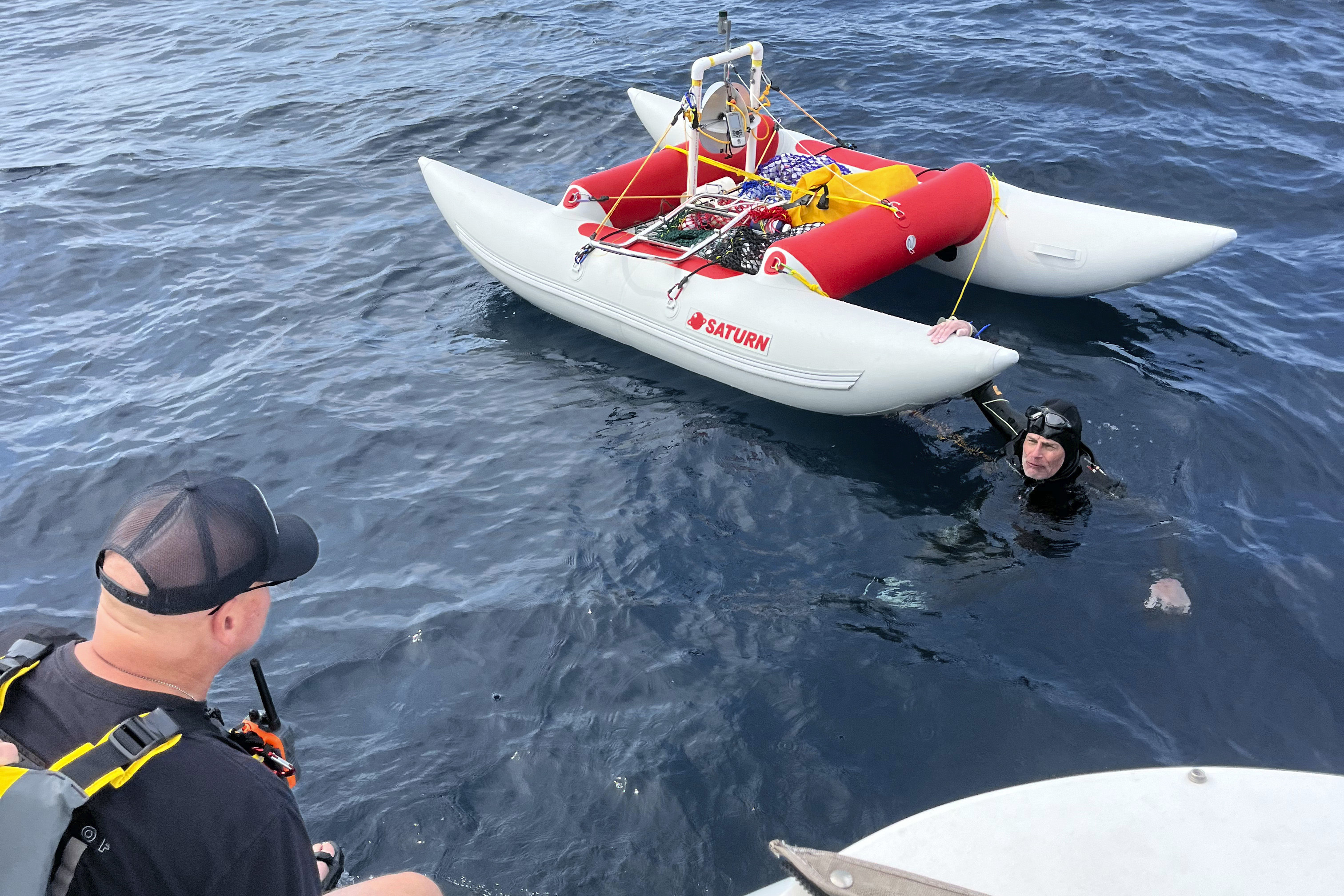 In this image provided by Jonathan Boeve, Jim Dreyer, right, talks to his support team in Lake Michigan, Thursday, Aug. 8, 2024, on the third day of his attempt to swim from Michigan to Wisconsin. 