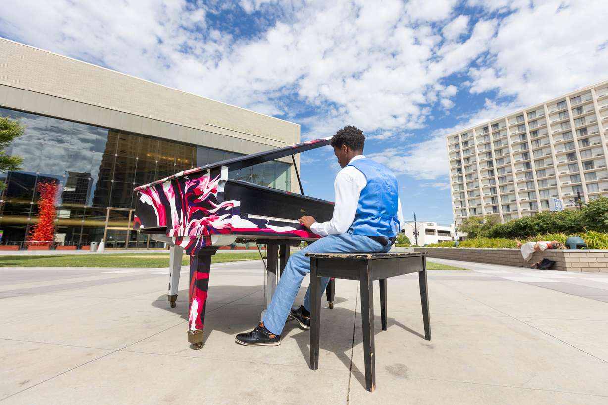Ozi Fryer, 14, from Logan, plays on the pianos in front of Maurice Abravanel Hall while his mother Melody Fryer rests in the background, in Salt Lake City on Aug. 4.