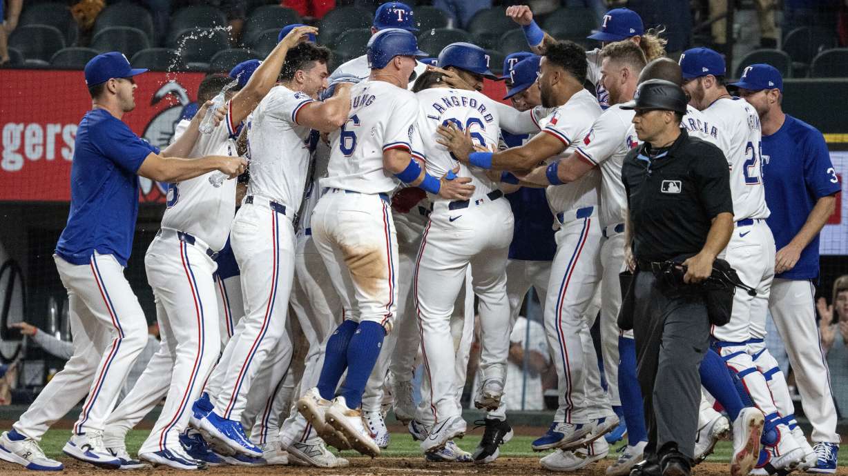 Wyatt Langford (36), de los Rangers de Texas, celebra con sus compañeros de equipo en el plato después de conectar un grand slam ante el lanzador relevista de los Yankees de Nueva York, Clay Holmes, durante la novena entrada de un juego de béisbol el martes 3 de septiembre de 2024, en Arlington, Texas. Leody Taveras, Josh Smith y Marcus Semien anotaron en la jugada.